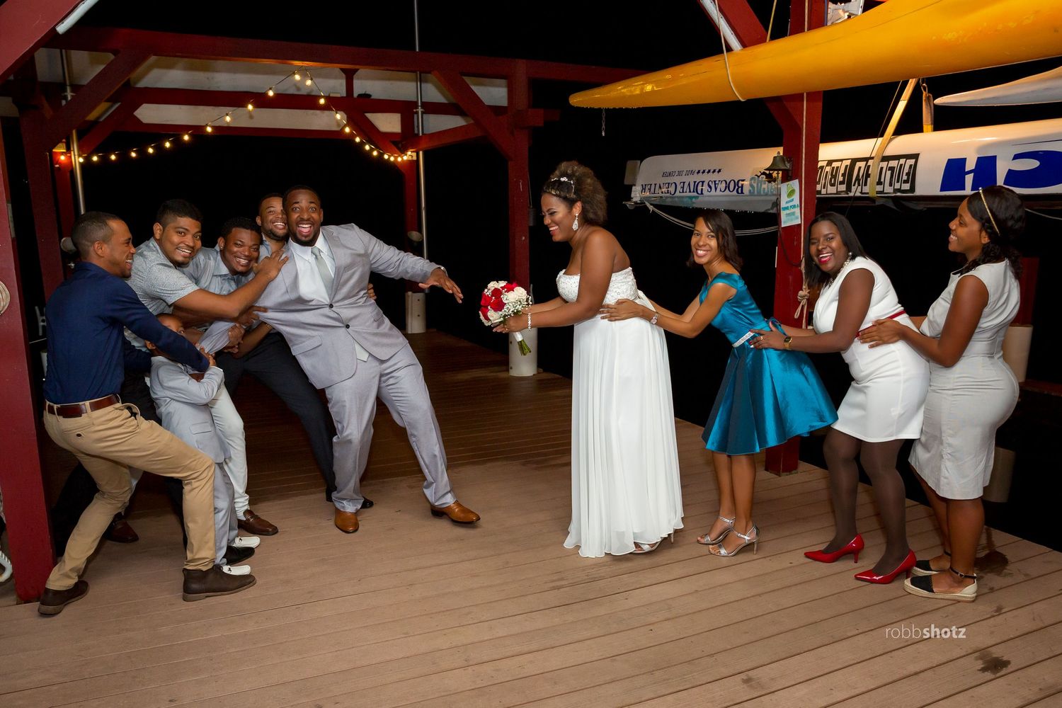 Wedding party dancing and celebrating on outdoor deck with string lights.