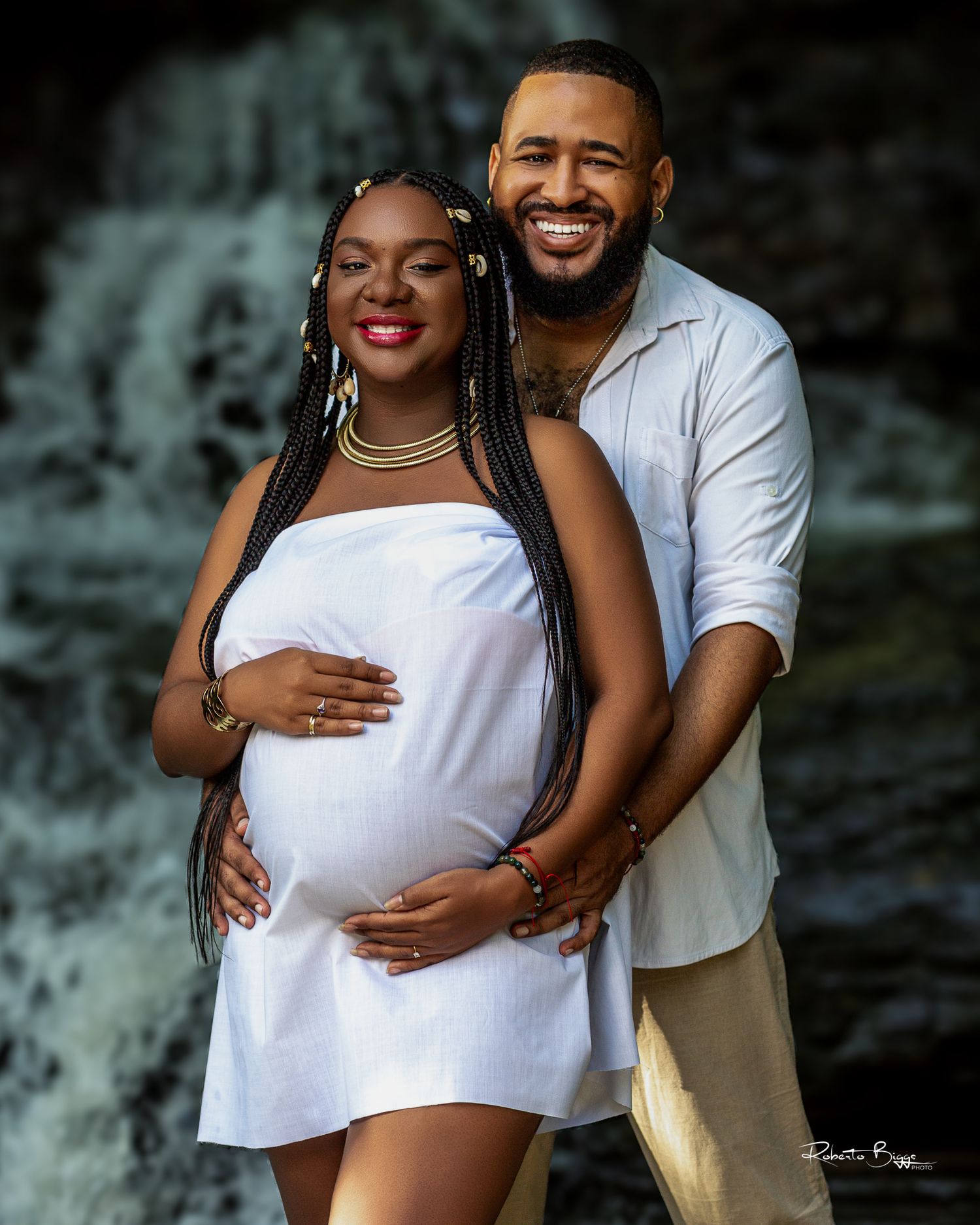 Maternity photo shoot with couple embracing against dark background.