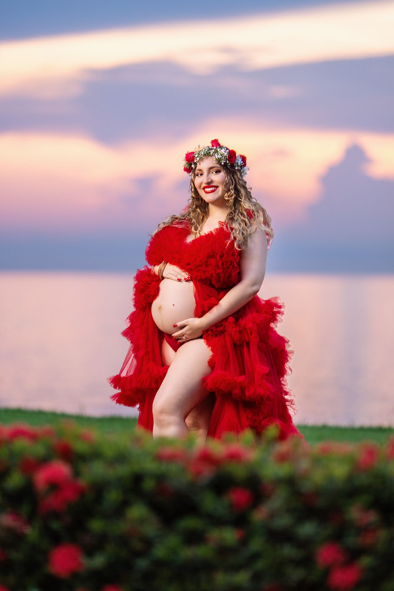 A maternity photoshoot in a field at sunset with red feathers and floral accessories creating a dramatic silhouette.