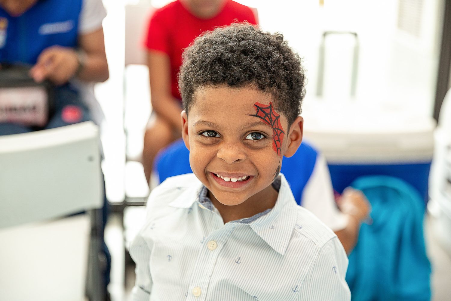 Smiling young boy with face paint design on cheek at a fun children's event.