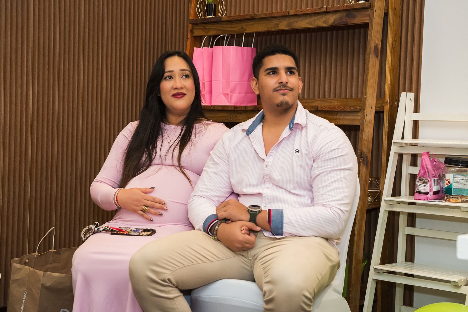 A couple in coordinating pink and white outfits sit together during a casual photo session.