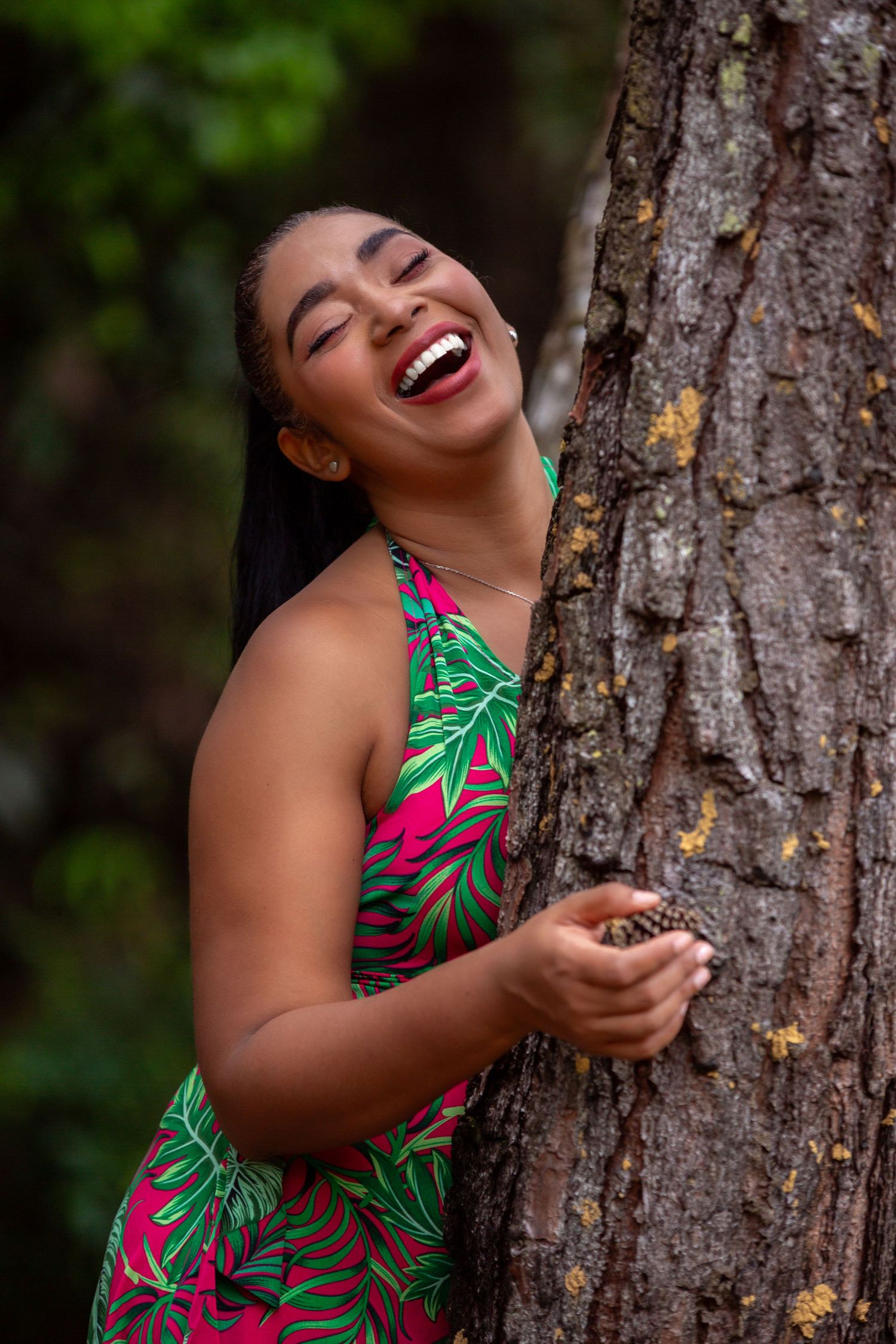 A candid portrait shows a happy person laughing while leaning against a tree trunk.