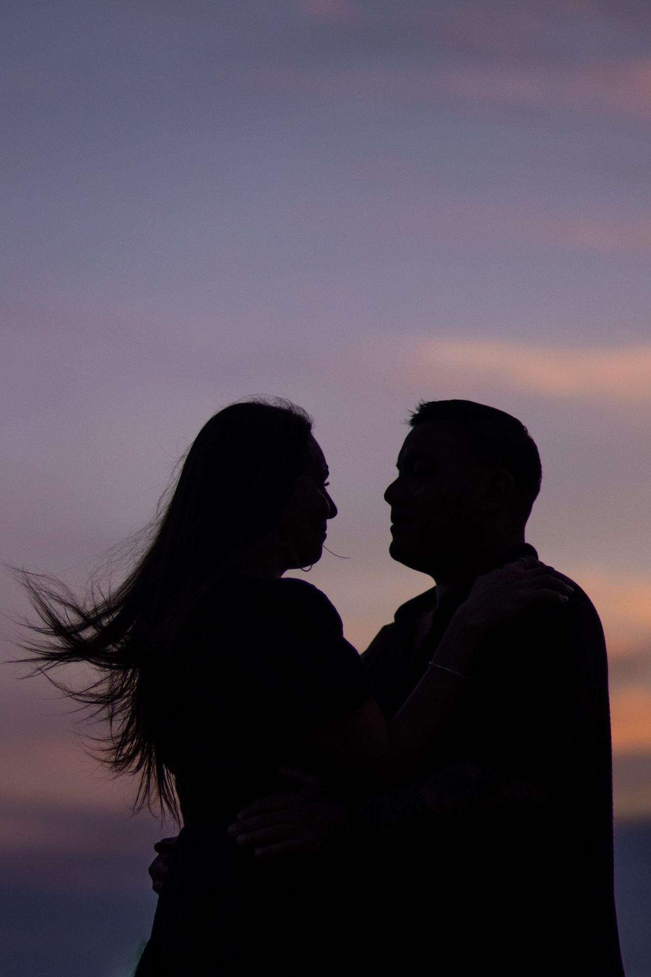 Romantic silhouette of a couple facing each other against a vibrant purple and pink sunset sky.