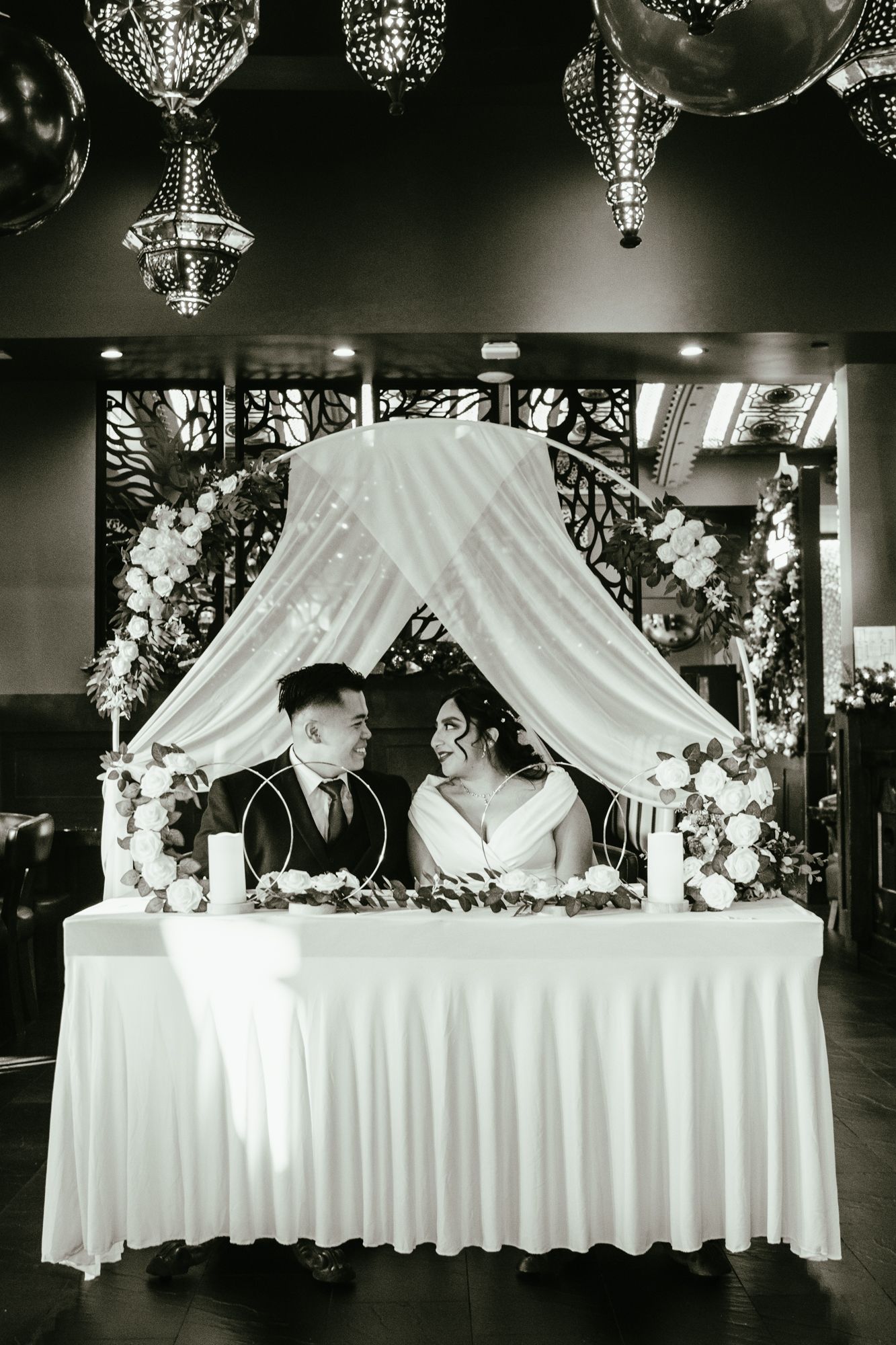 Bride and groom at sweetheart table under canopy with floral decor in black and white.