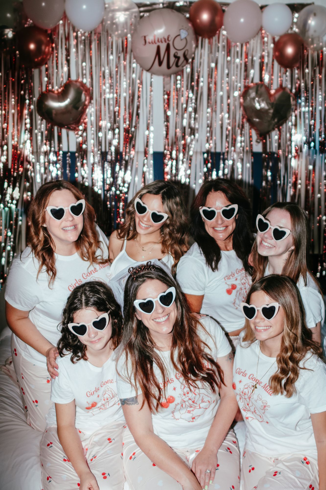 Group of seven women in matching pajamas and heart sunglasses at a festive bachelorette party.