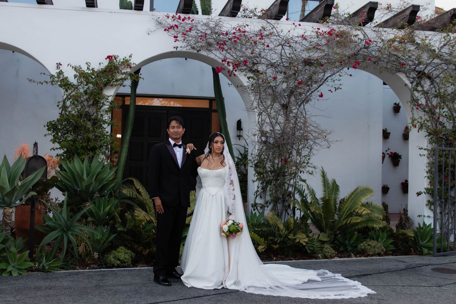Bride and groom posing under floral arch at elegant outdoor wedding venue with lush greenery.