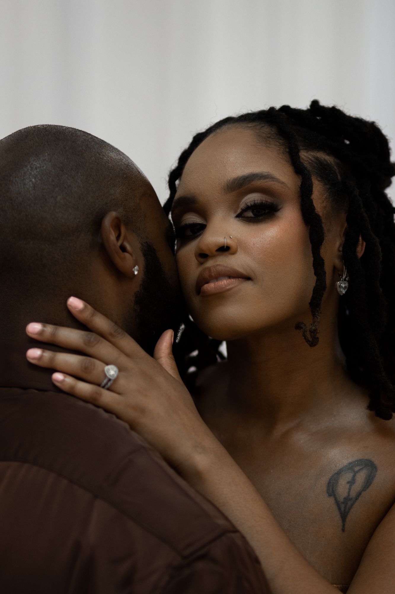 Close-up of Black bride with dramatic eye makeup and diamond ring embracing groom in intimate portrait.