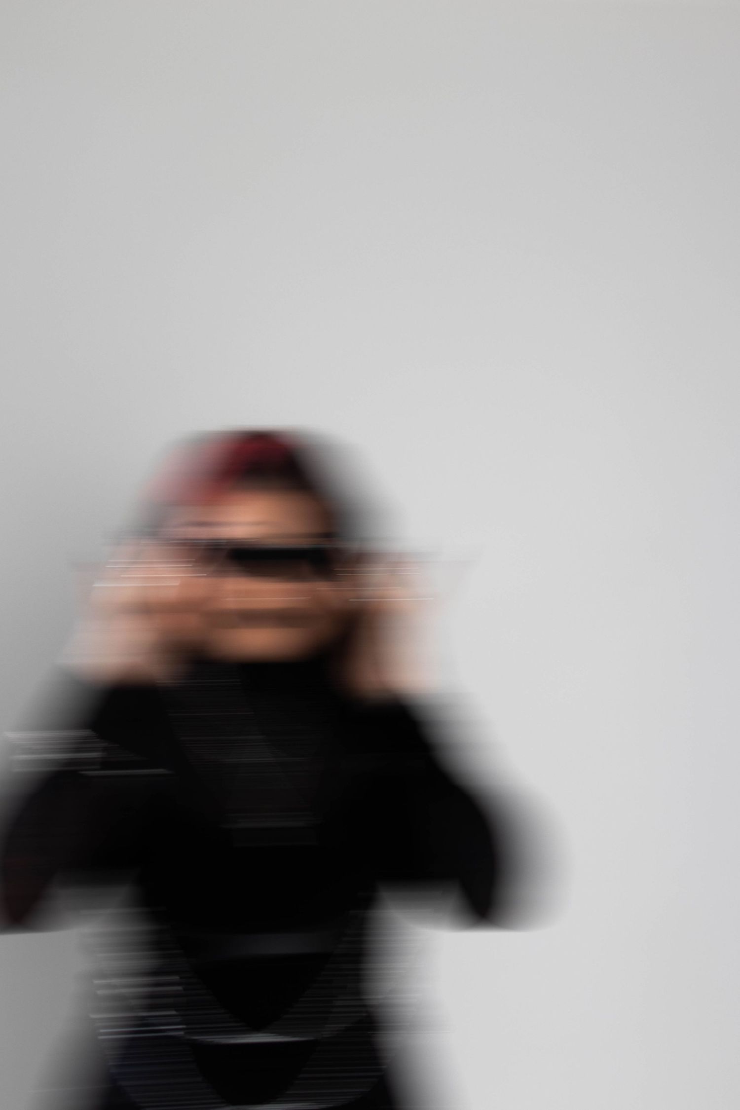Artistic blurred motion photo of a person in black outfit against a light gray background.
