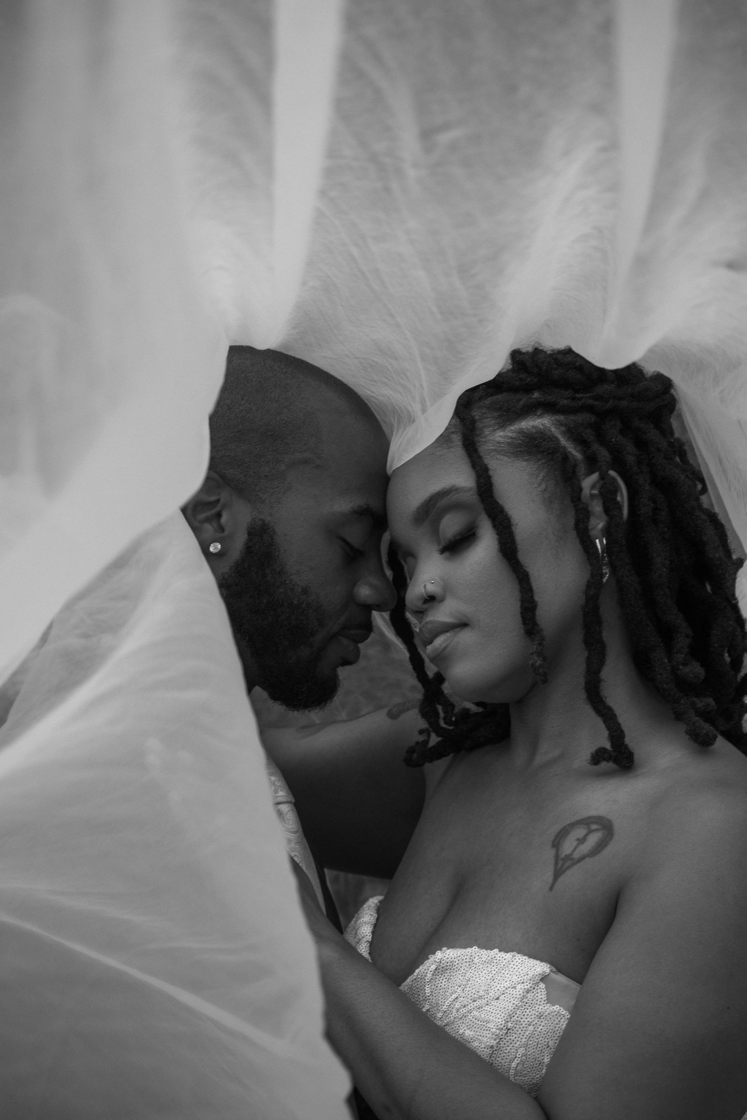 Romantic black and white portrait of a bride and groom embracing under a flowing wedding veil.