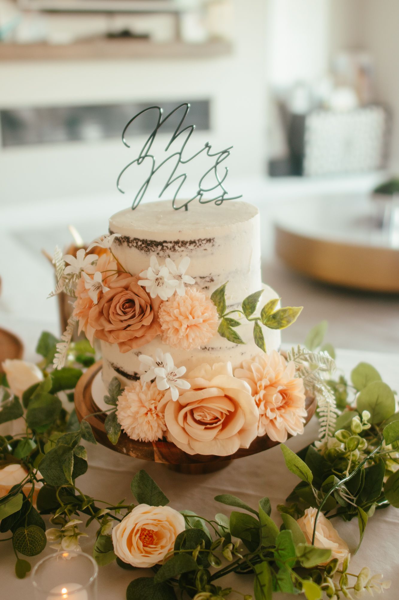 Two-tier semi-naked wedding cake topped with Mr and Mrs topper, adorned with peach roses and greenery garland.