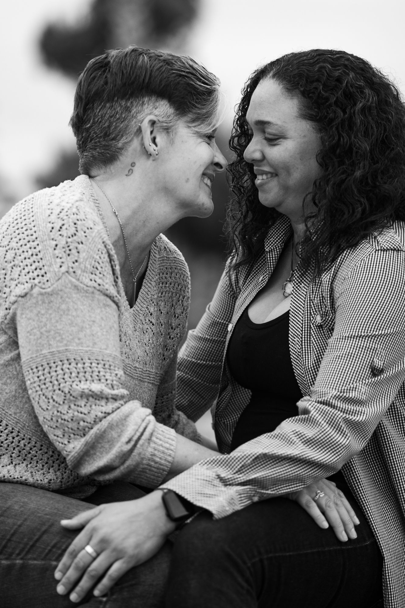 A black and white photo of two women smiling and leaning close together outdoors.