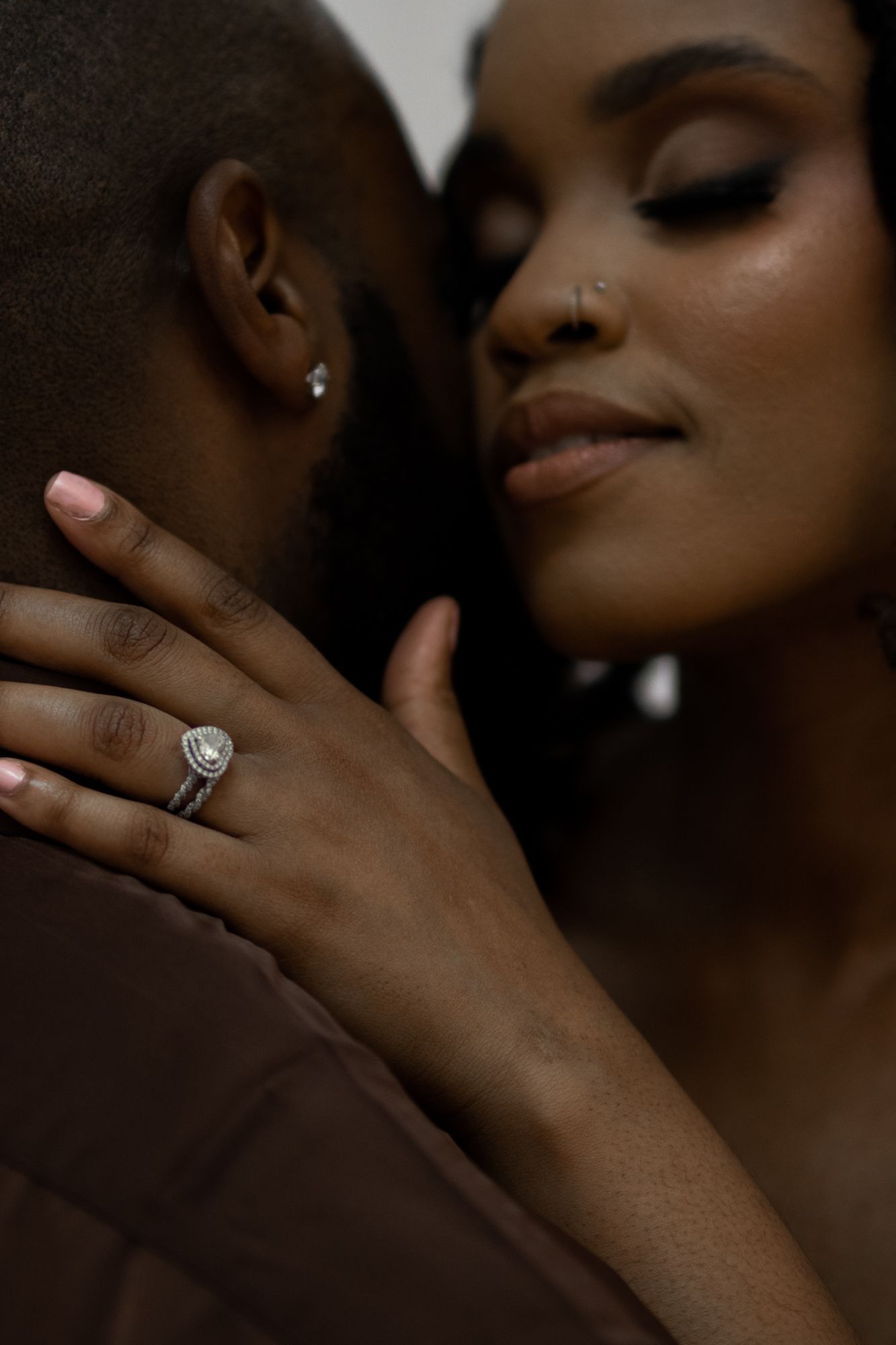 Close-up of a bride smiling with a halo diamond engagement ring resting on her partners shoulder.