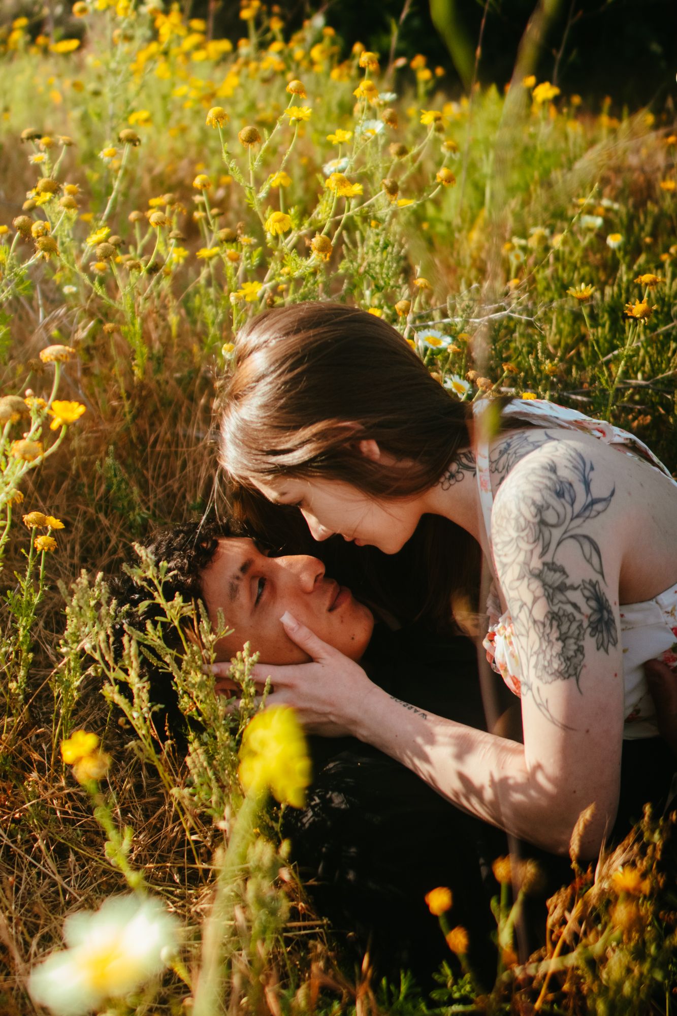 Romantic couple lying in sunny wildflower field with yellow blooms, woman tenderly holding man's face.