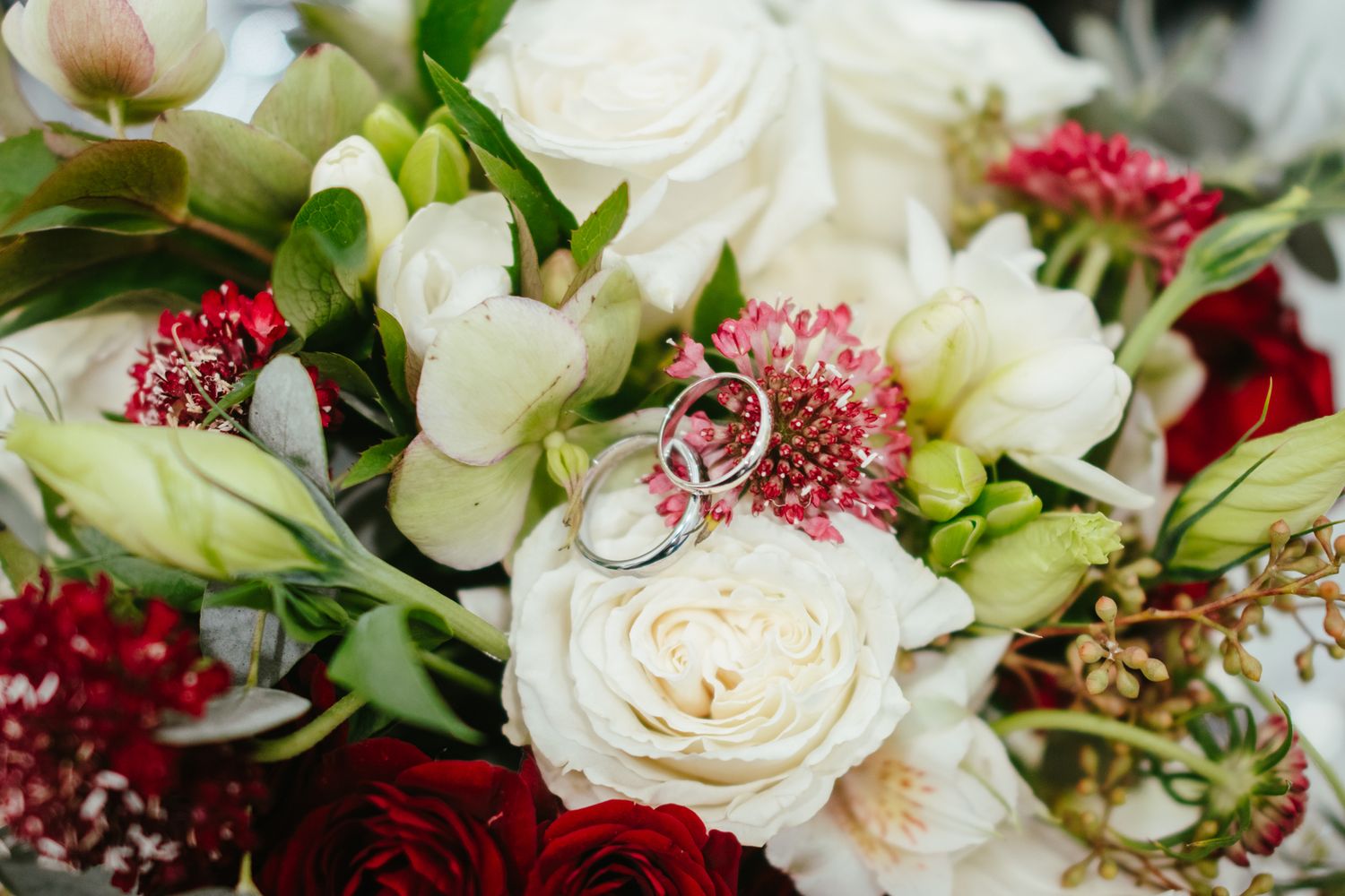 Wedding rings resting on a bouquet of white roses and red flowers.