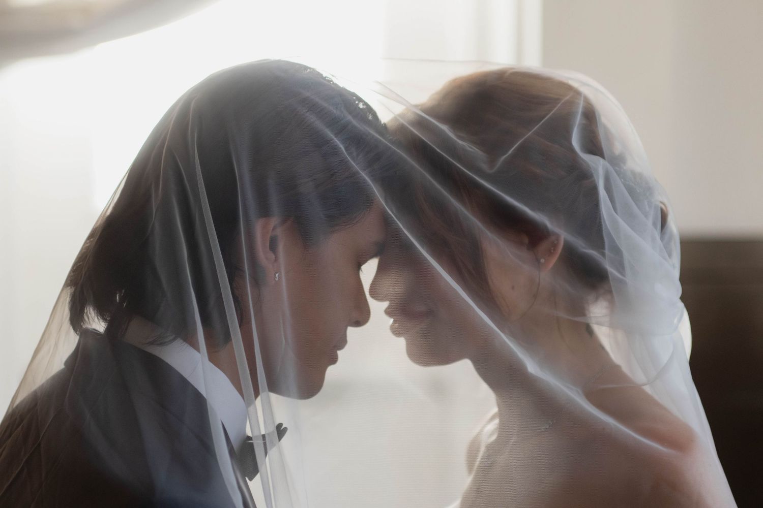 Bride and groom sharing an intimate moment under a flowing white veil on their wedding day.