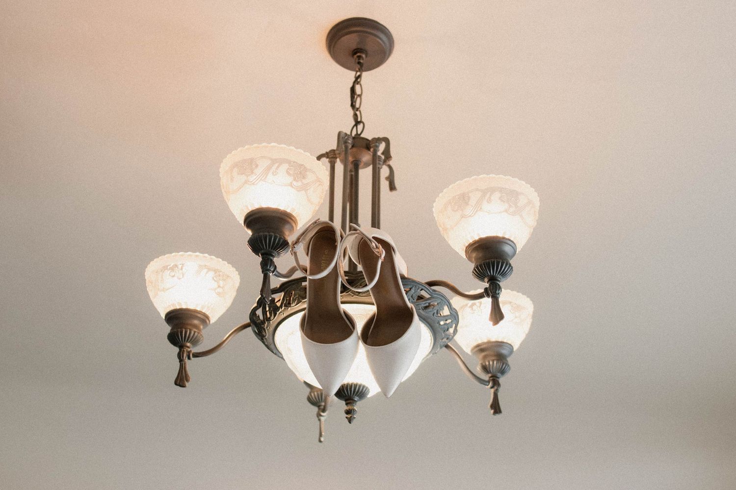 Vintage brass chandelier with frosted etched glass shades hanging from a white ceiling.
