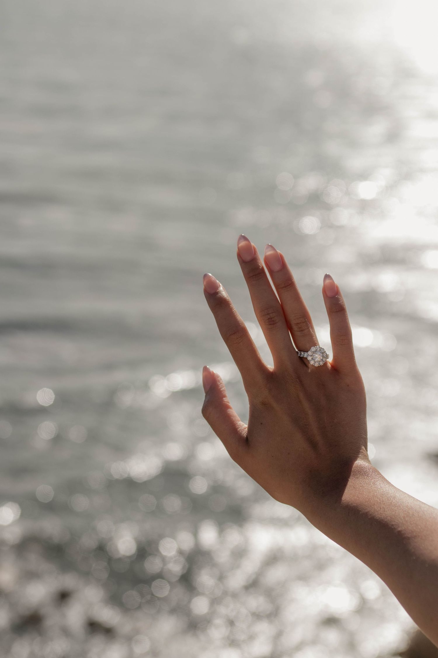 Close-up of bride's hand displaying large diamond engagement ring with shimmering water background.