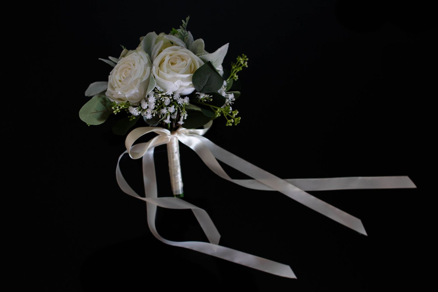 Elegant white rose bridal bouquet tied with satin ribbon on a dark background.