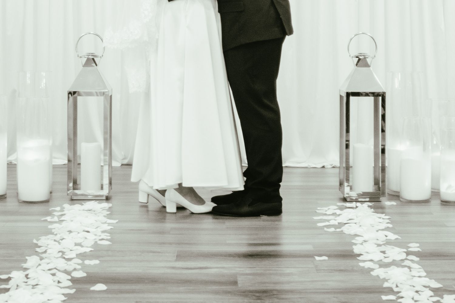 Bride and groom stand together at altar flanked by white lanterns and rose petal aisle runner.