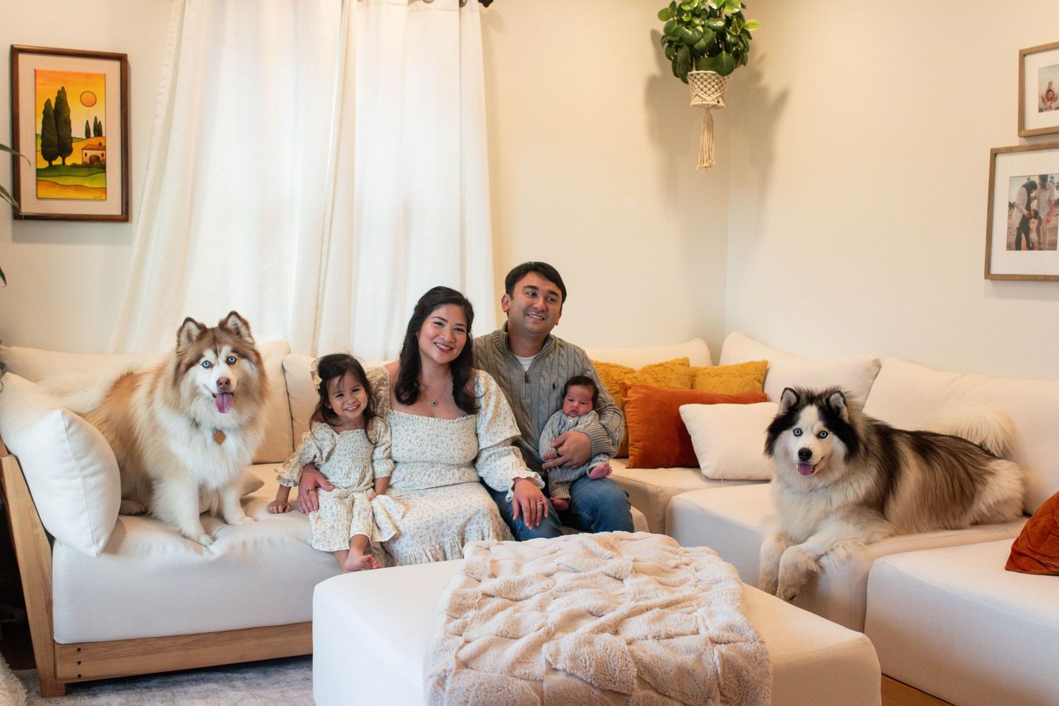 Happy family with two Alaskan Malamute dogs posing together on a cozy living room sofa.