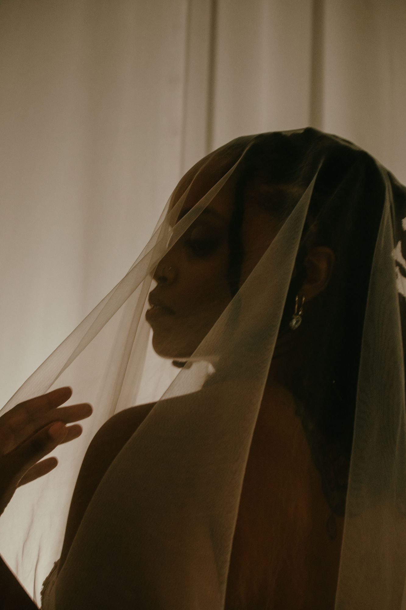 Dramatic silhouette of a bride wearing a sheer wedding veil in warm golden light.