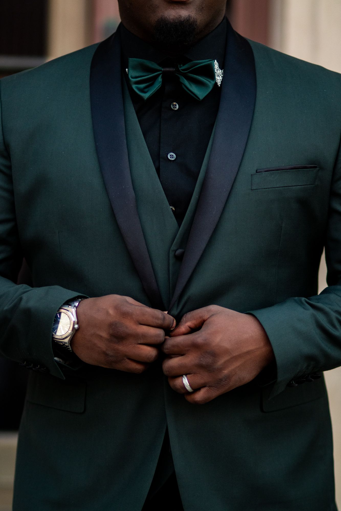 Groom in elegant dark green tuxedo with matching bow tie and silver watch buttoning his jacket.