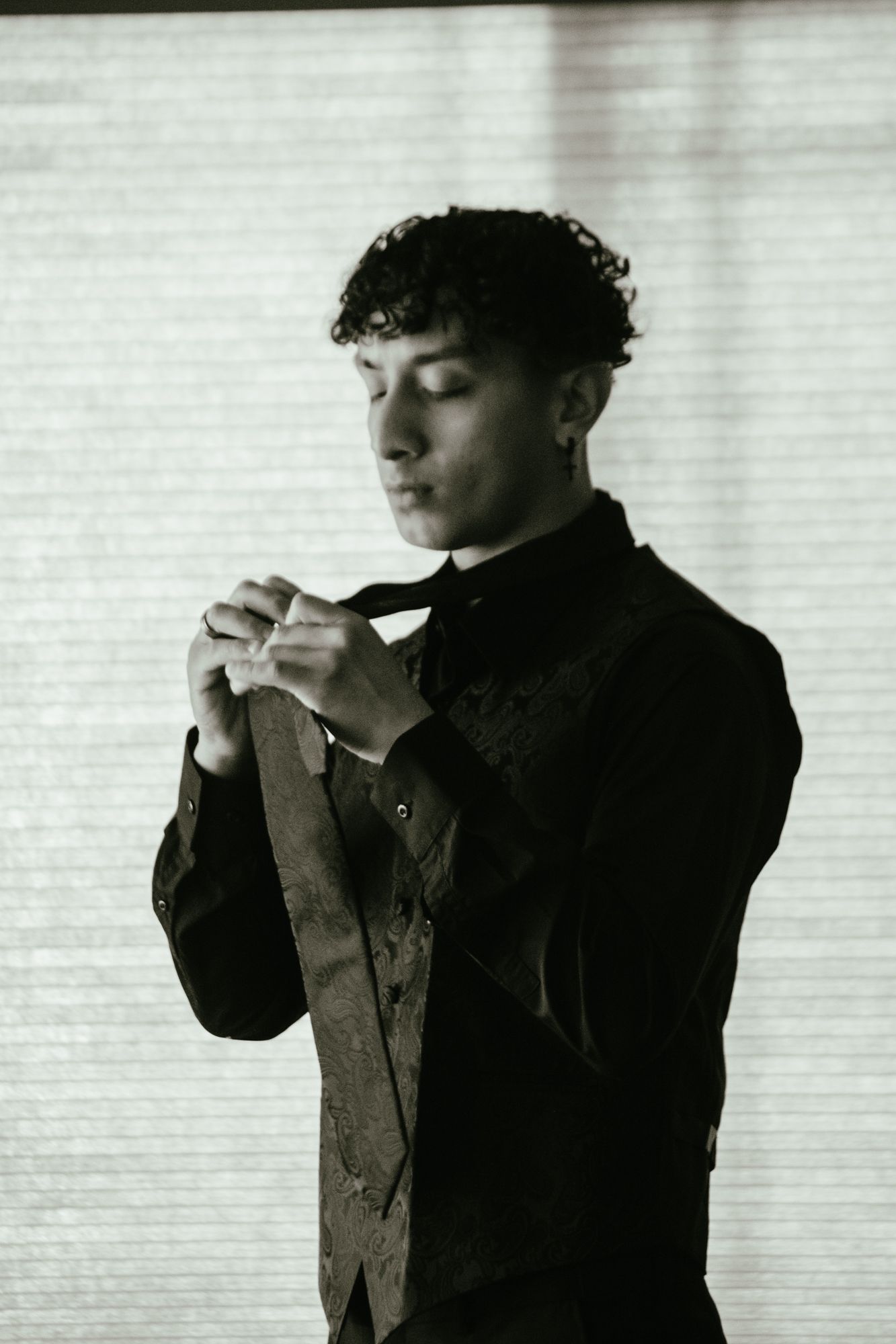 Black and white portrait of young groom adjusting tie before wedding ceremony.