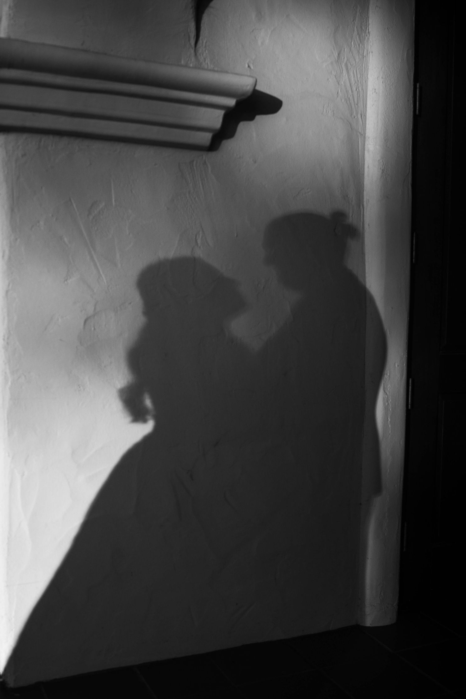 Romantic black and white shadow of bride and groom on textured white wall.