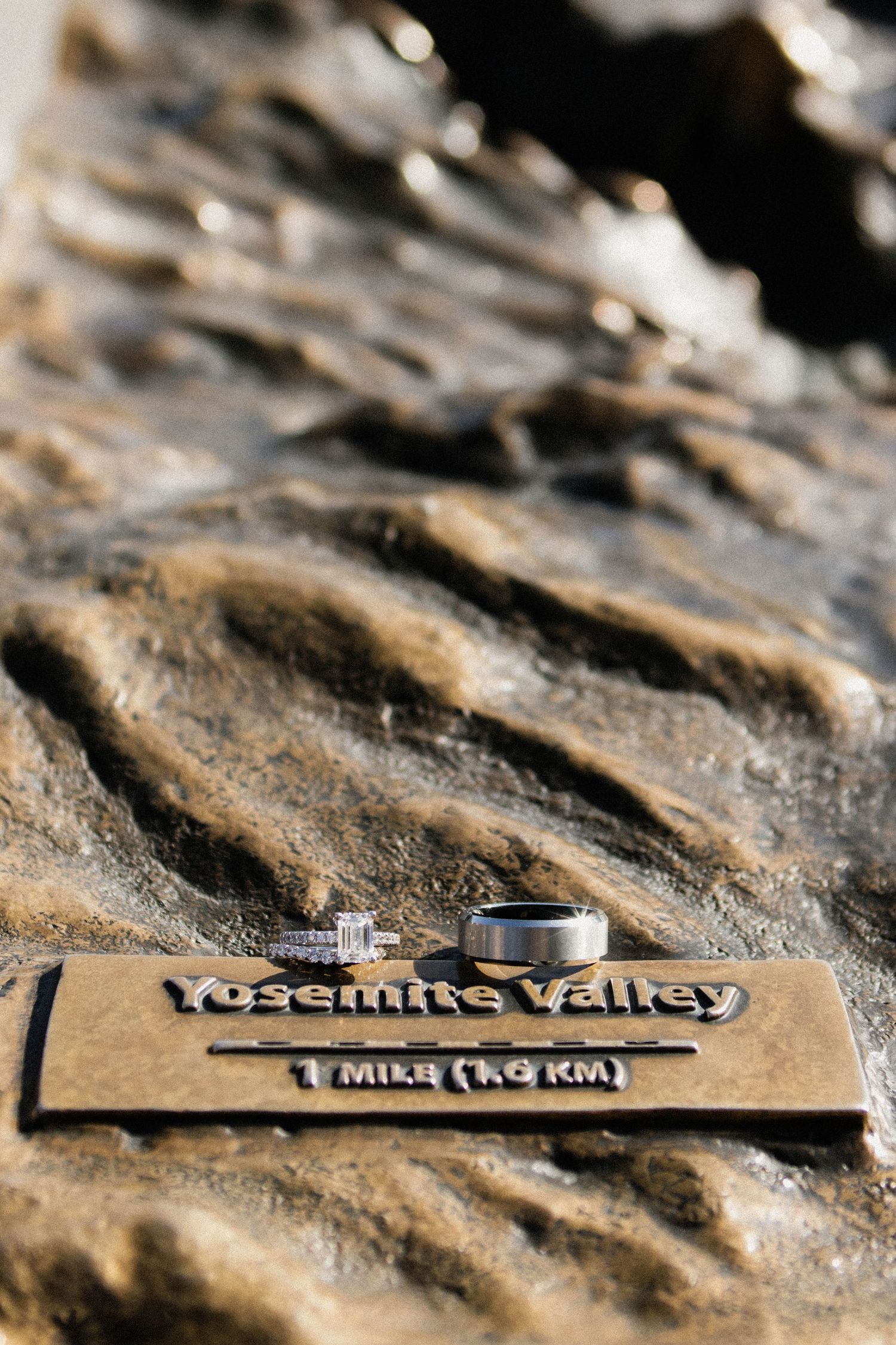 Wedding rings displayed on Yosemite Valley 1 mile marker sign on textured rock surface.