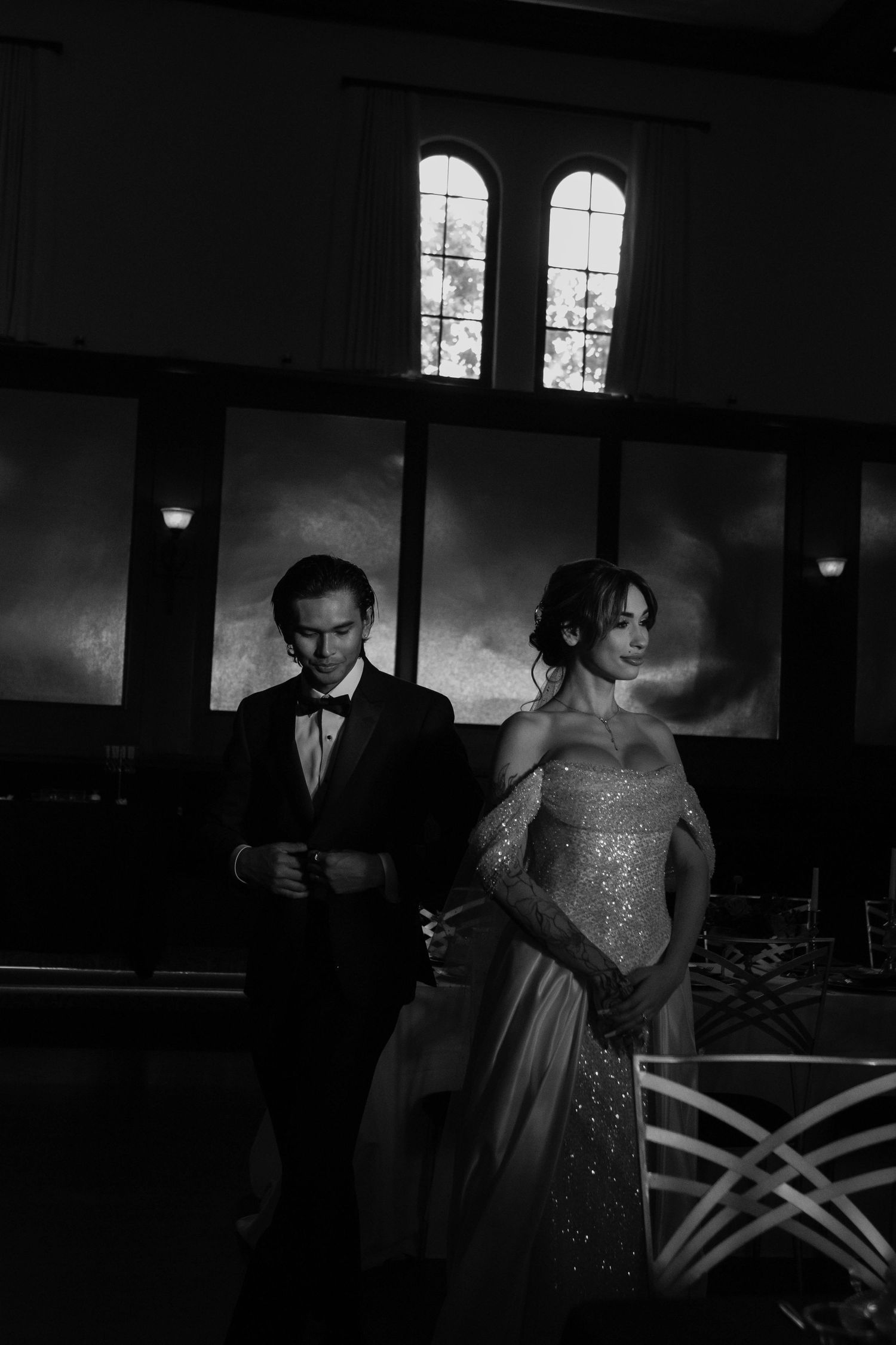 Black and white photo of an elegant bride in a sequined gown and groom in a tuxedo at a wedding reception.