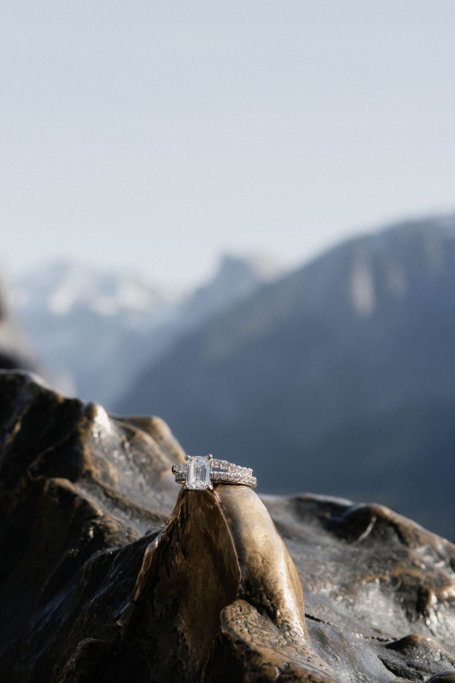 Diamond engagement ring displayed on rocky surface with mountain valley backdrop.