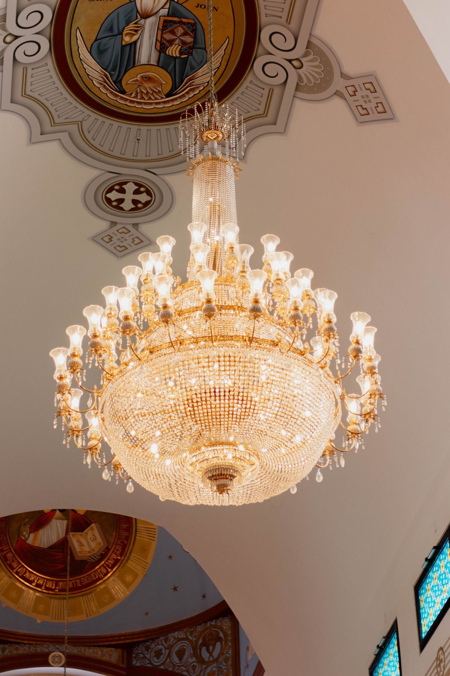 Ornate gold crystal chandelier hanging in an Orthodox church with religious icons and decorative ceiling artwork.