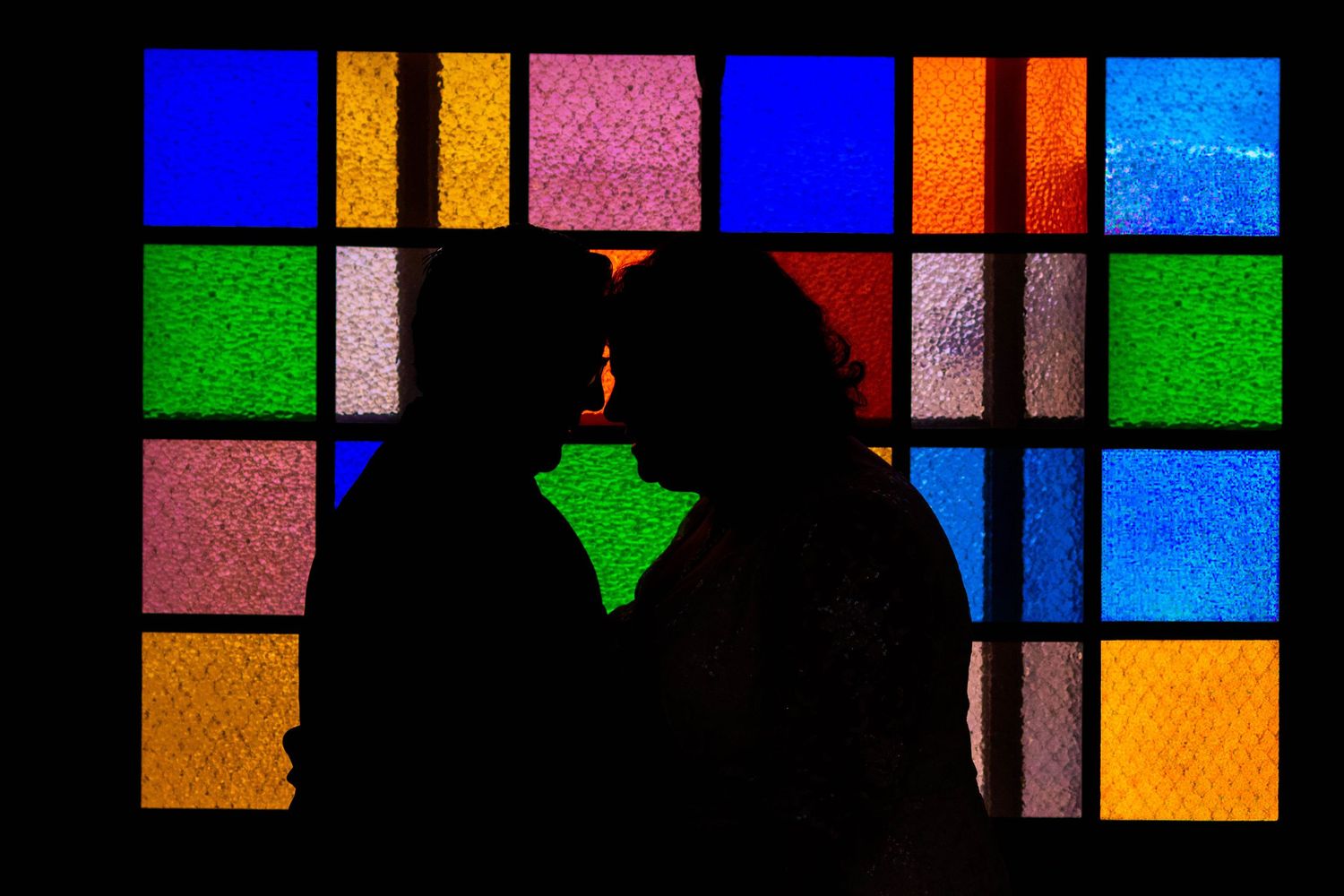 Romantic silhouette of couple about to kiss backlit by colorful stained glass window panels.