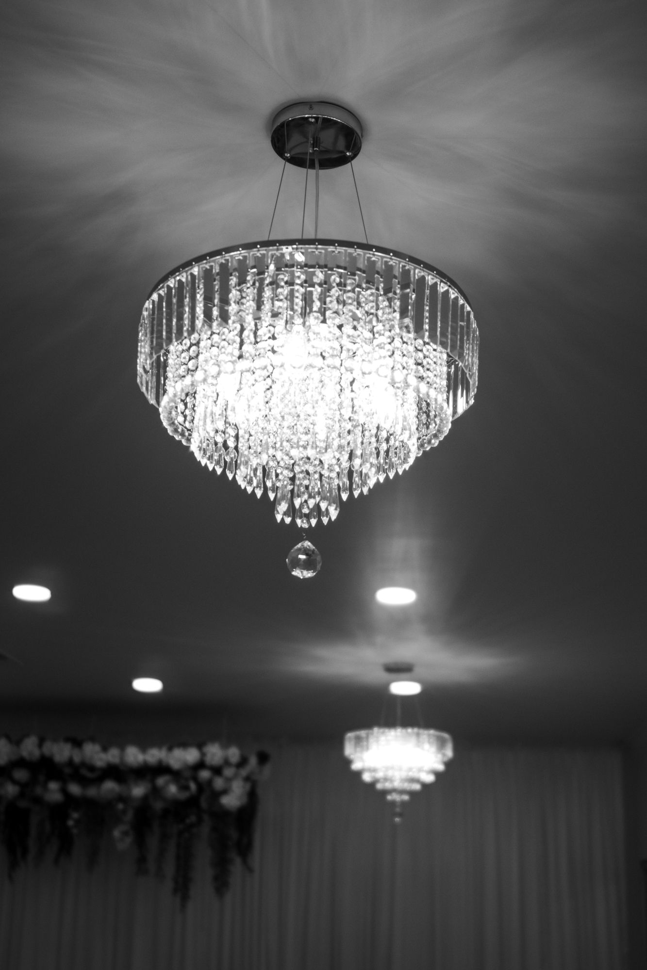 Elegant crystal chandelier glowing in black and white at a wedding venue.