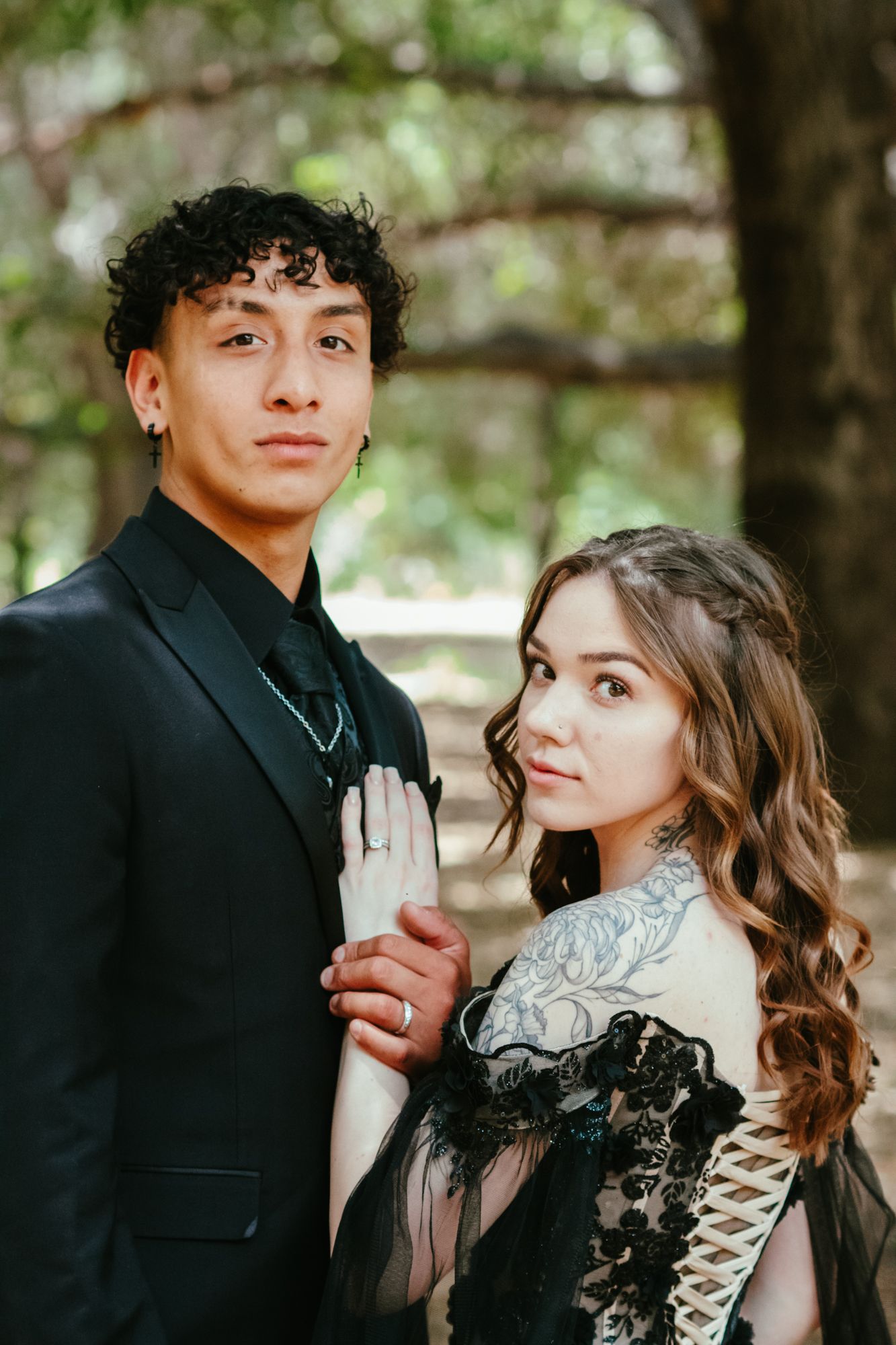 Couple in black wedding attire posing outdoors, groom in suit and bride in black lace gown.