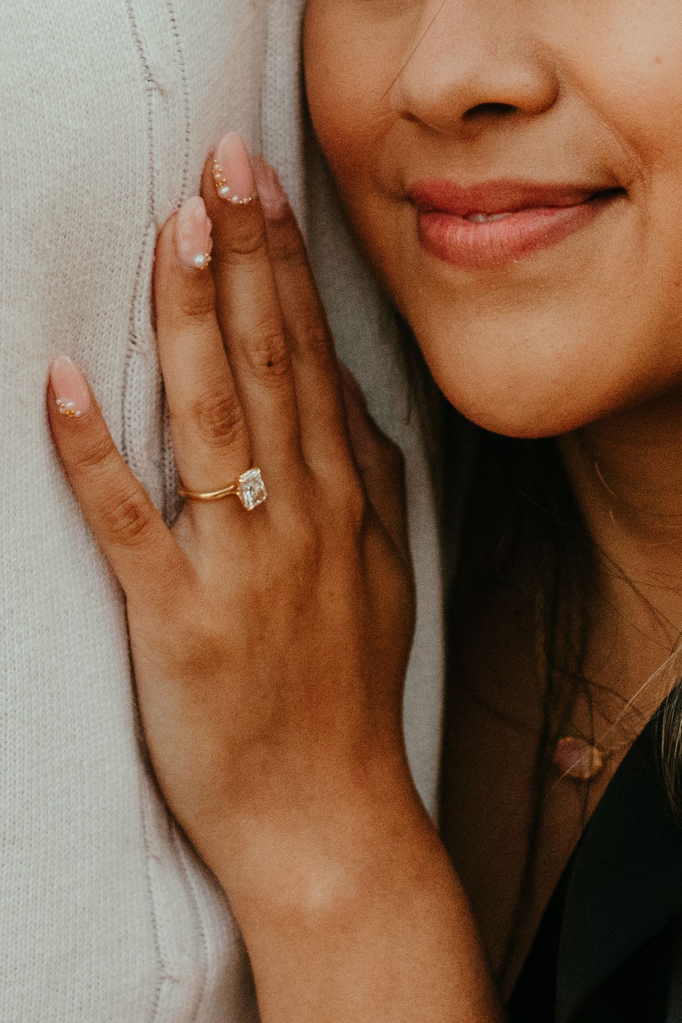 Close-up of a woman smiling wearing a gold solitaire diamond engagement ring with nude manicured nails.