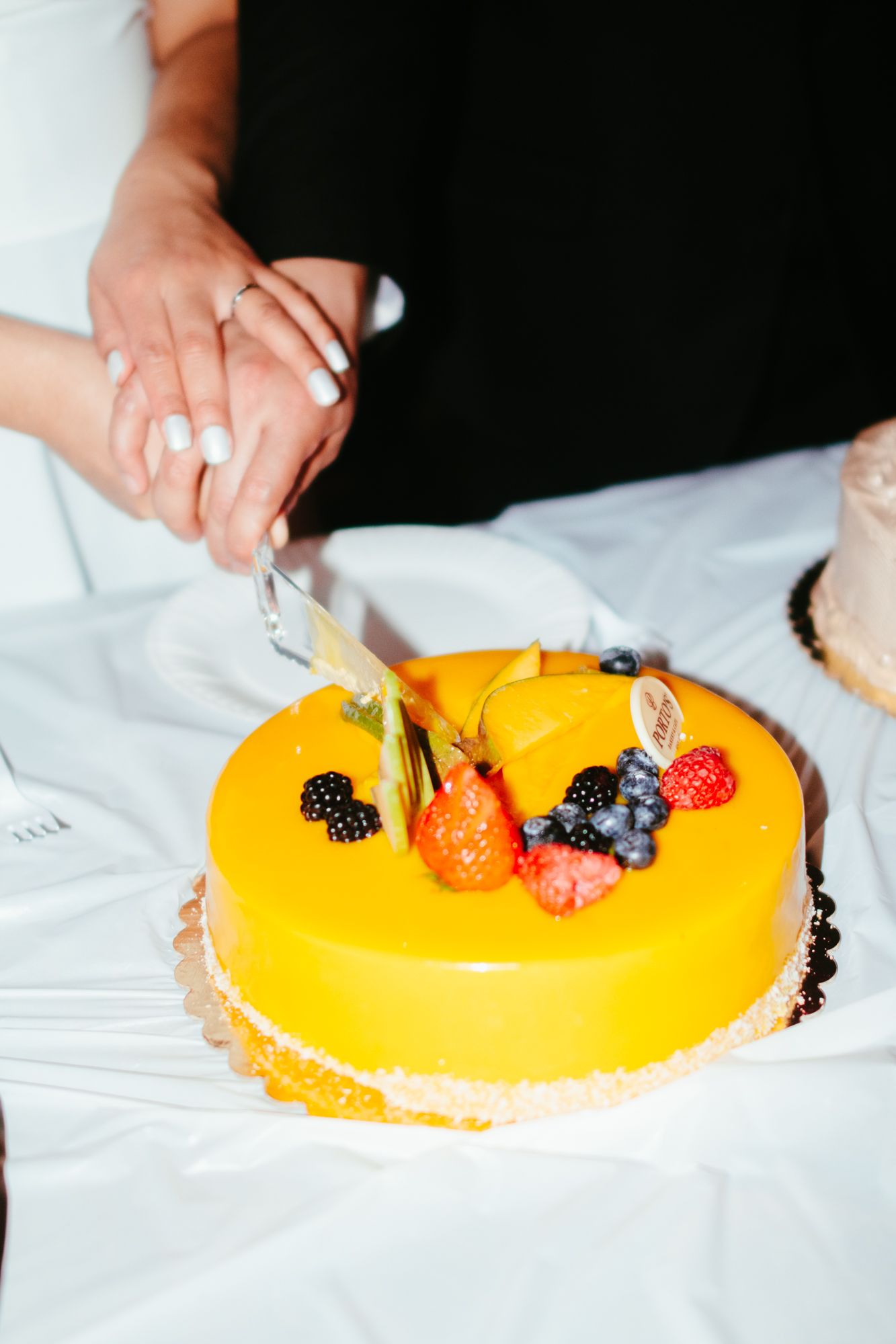 Bride and groom cutting a yellow mirror glaze wedding cake topped with fresh berries.
