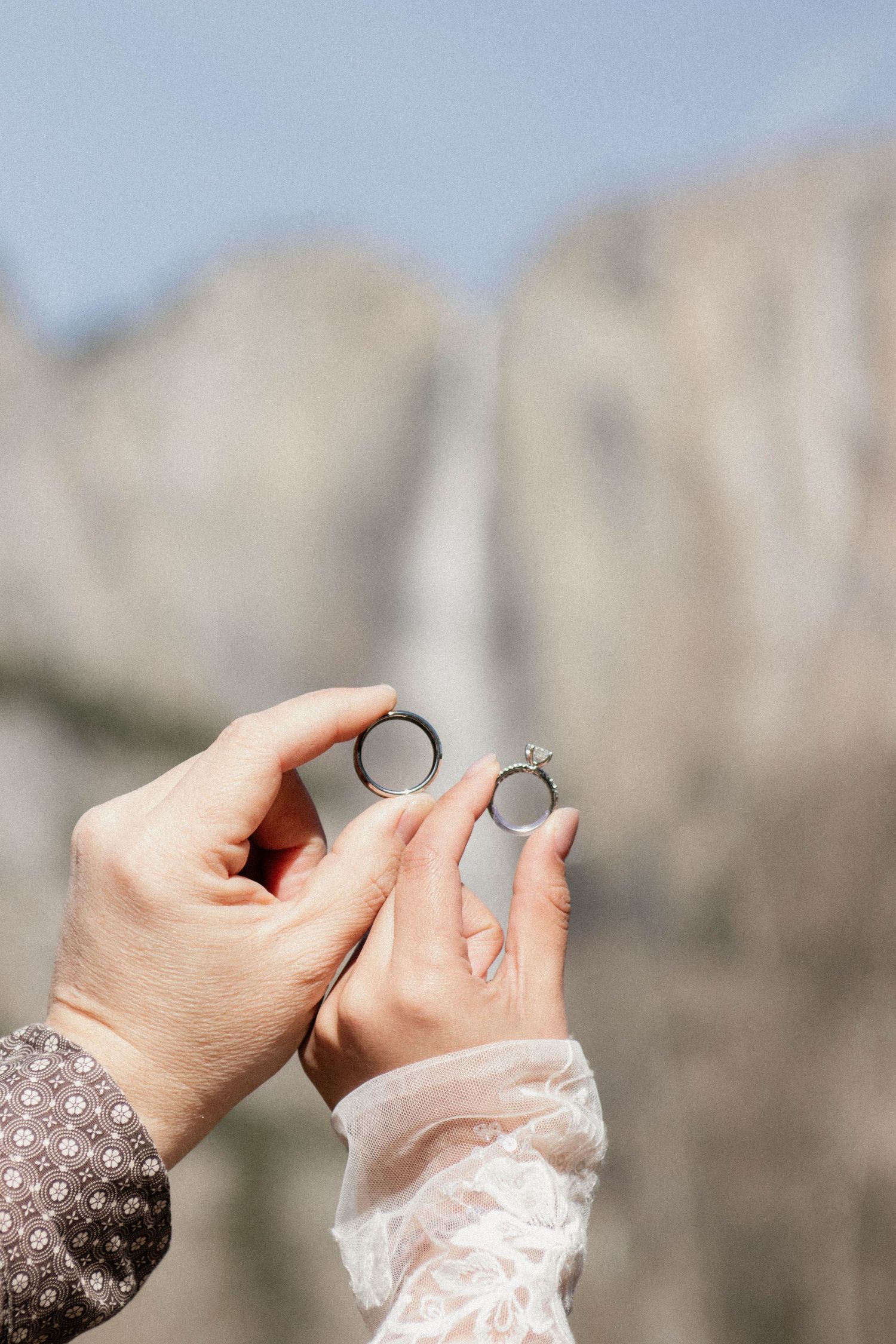 Two hands holding wedding rings with Yosemite Falls waterfall in the background.
