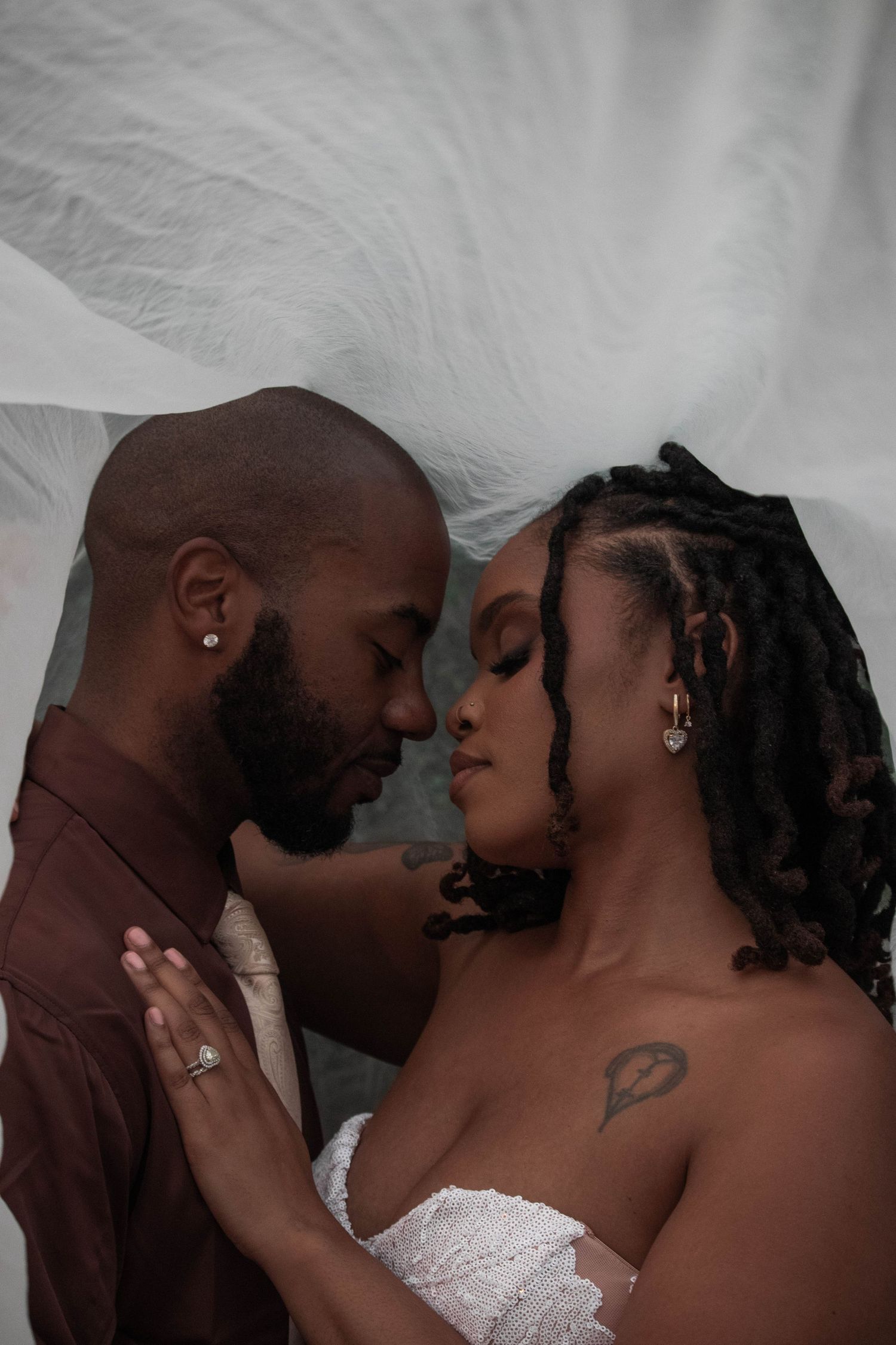 Romantic close-up of African American bride and groom almost kissing beneath a flowing white veil.