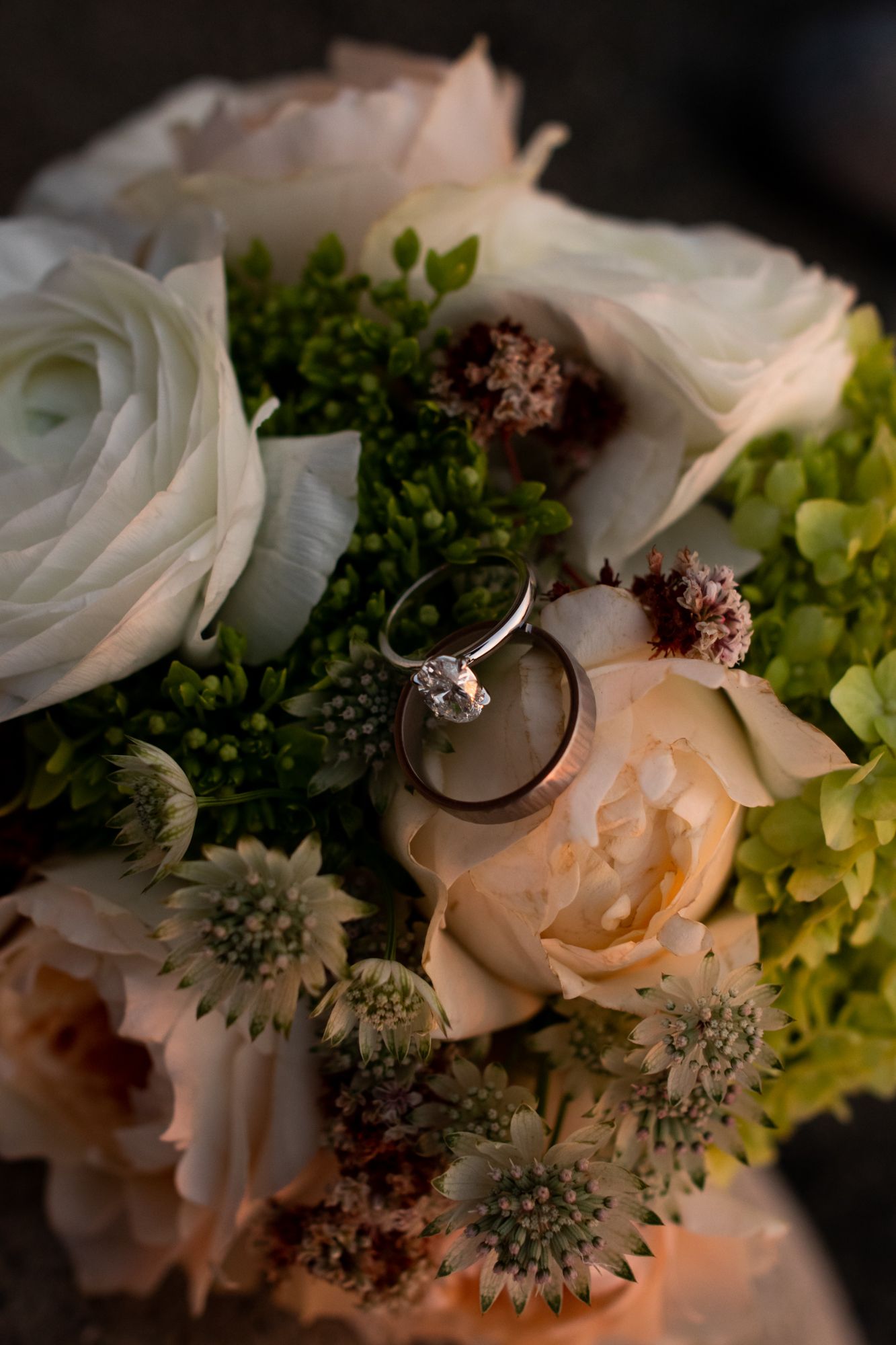 Diamond engagement ring and wedding band resting on a romantic bridal bouquet of white and peach roses.