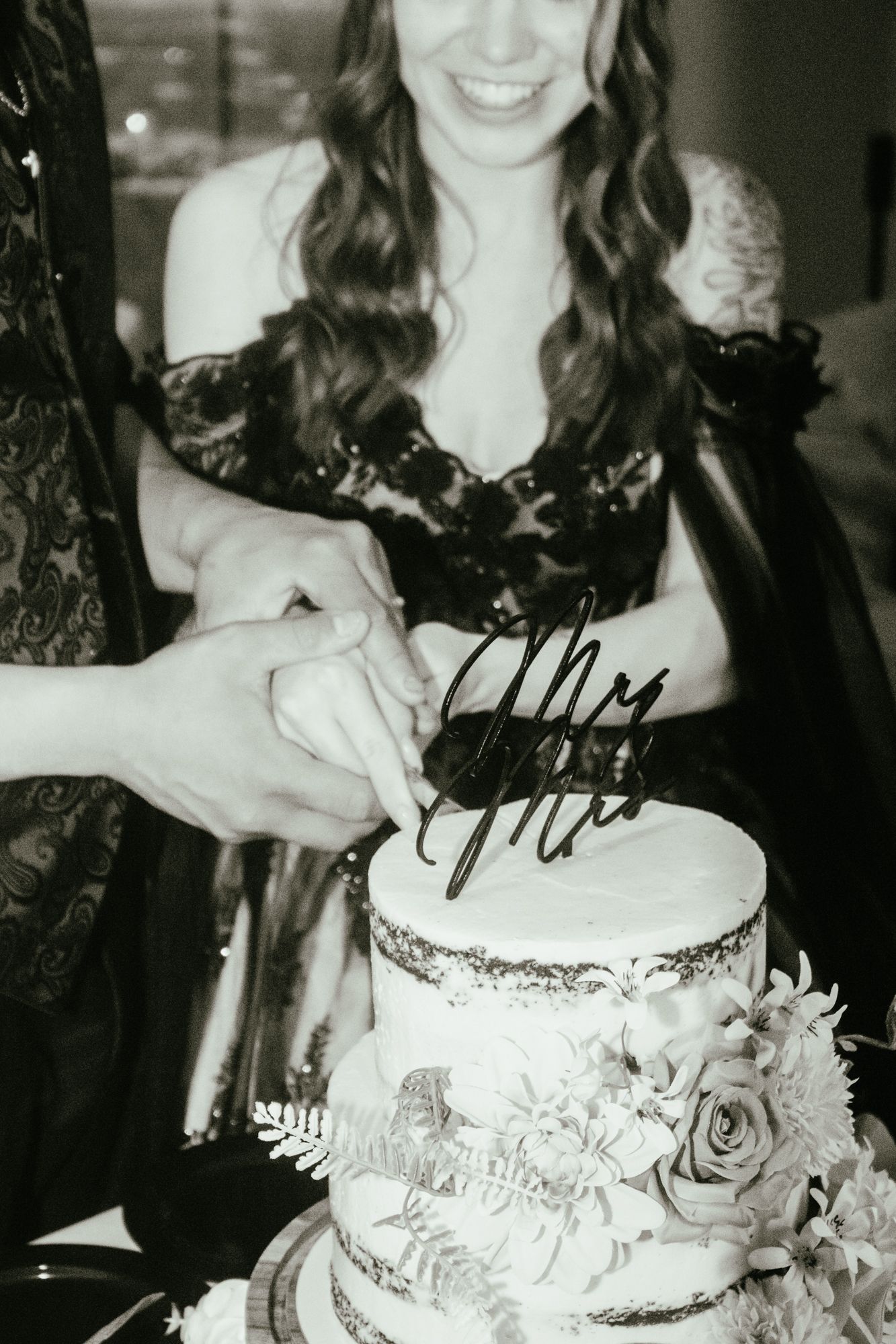 Couple cutting tiered wedding cake with Mr and Mrs topper in black and white photo.
