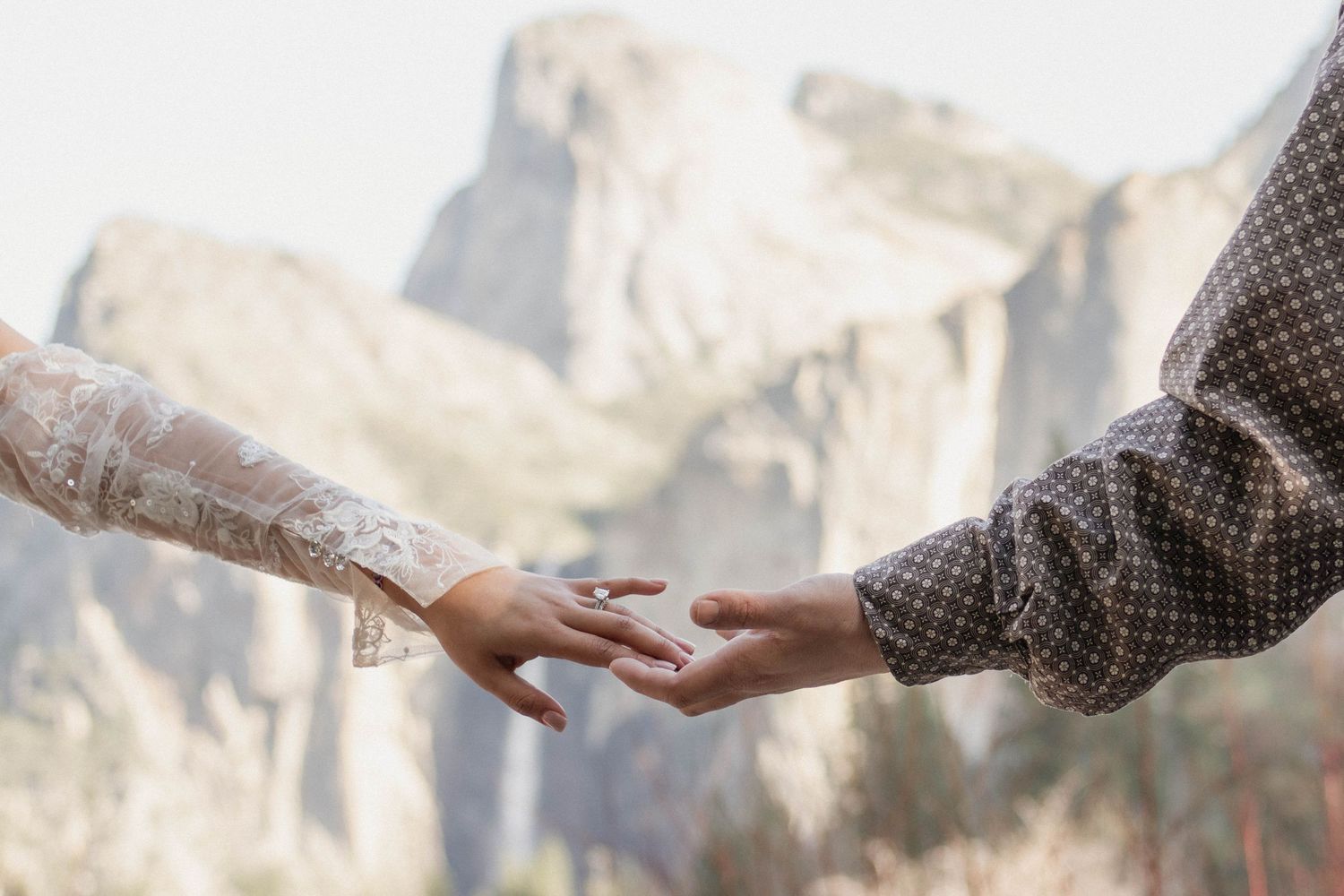 Bride and groom reaching for each other's hands with Yosemite Valley mountains in background.