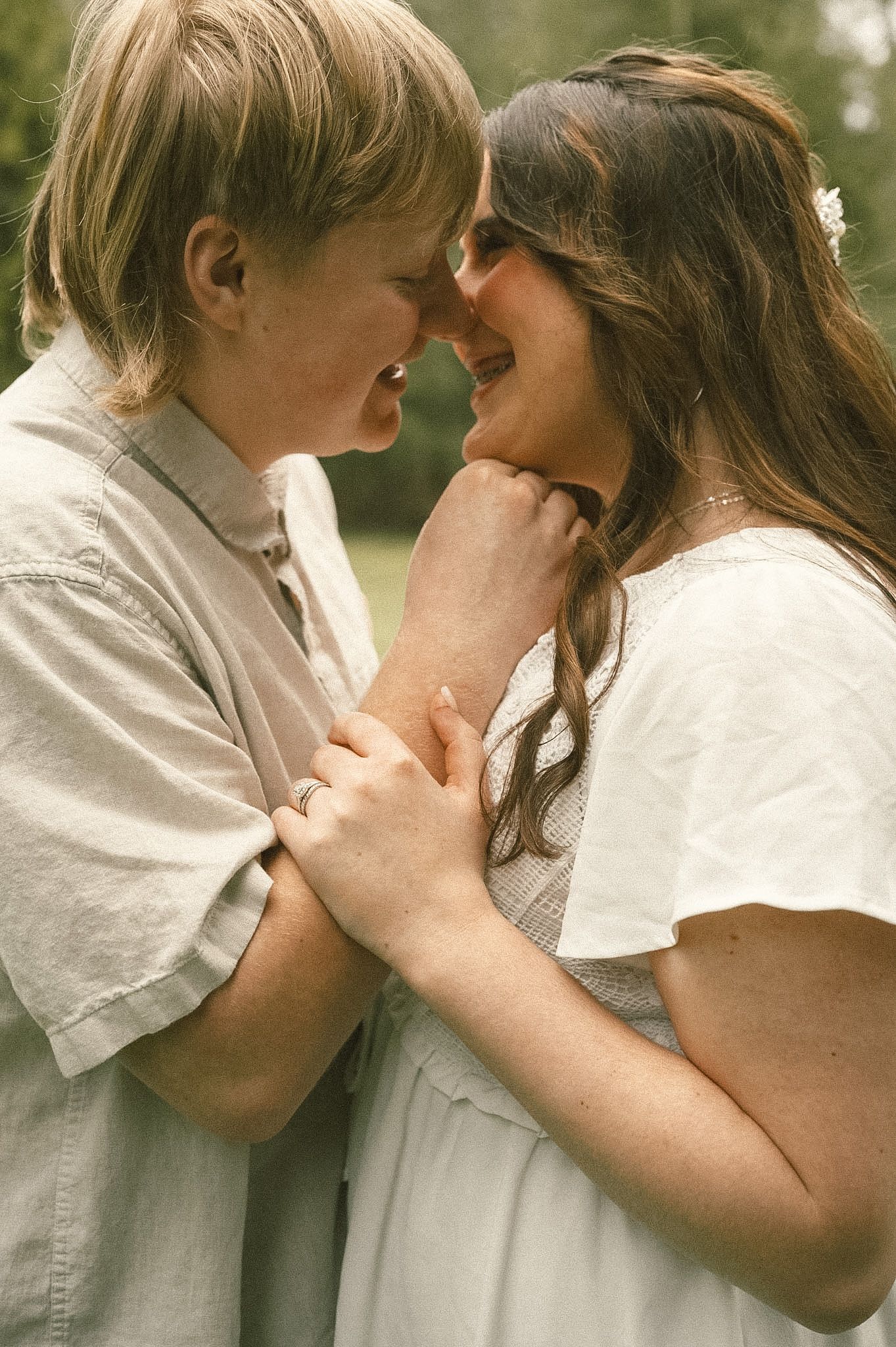 A couple smiling and holding hands closely together outdoors in a tender, romantic moment.
