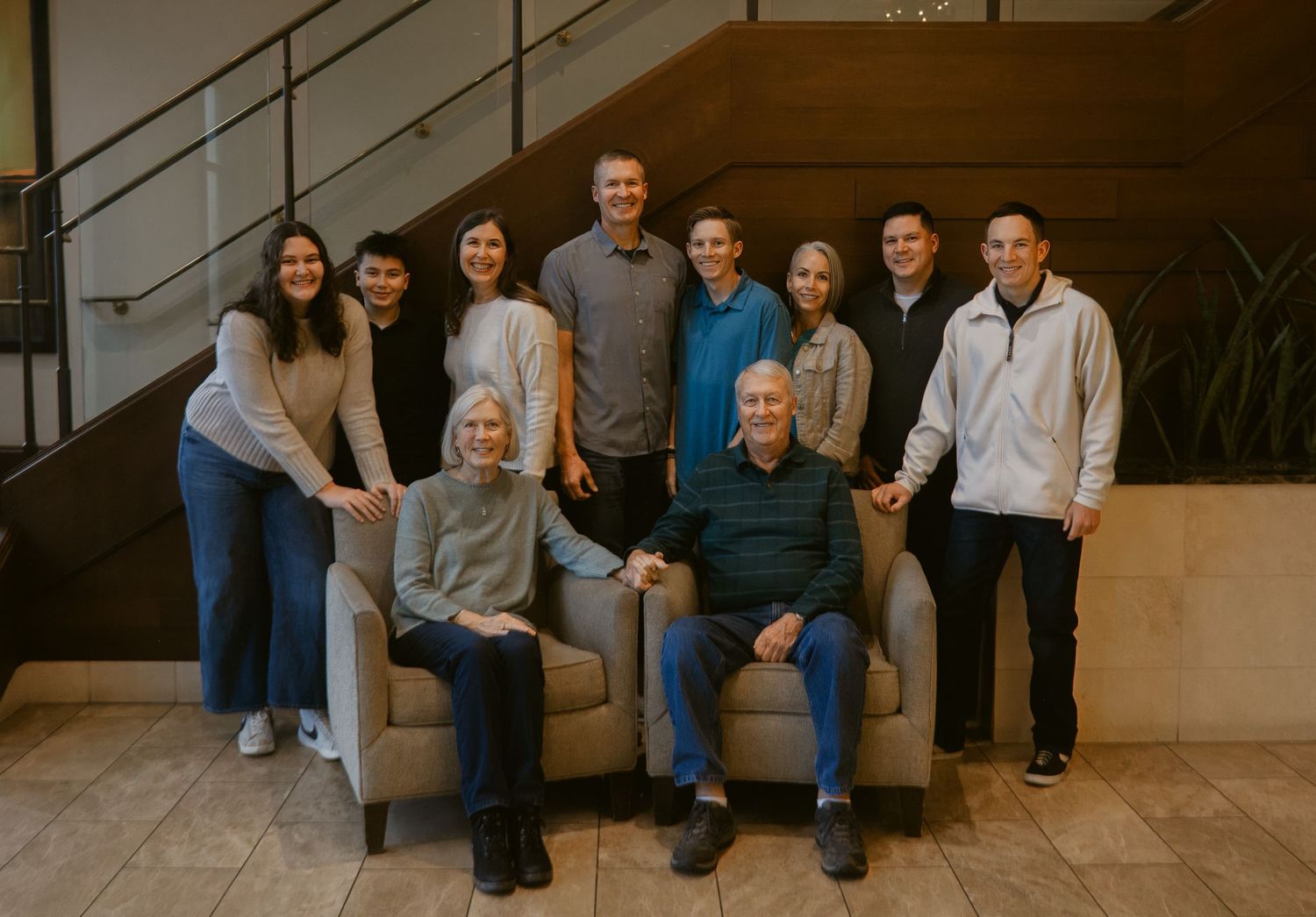 Large multigenerational family poses together on a staircase landing, with two grandparents seated in front of smiling relatives.
