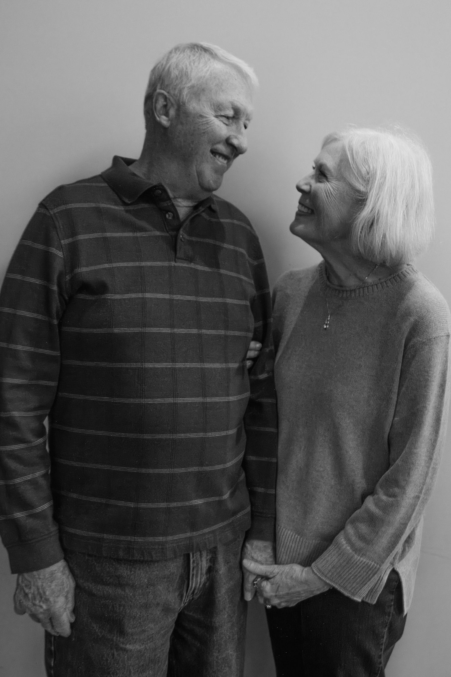 Black and white portrait of a smiling elderly couple standing close together and gazing warmly at each other.