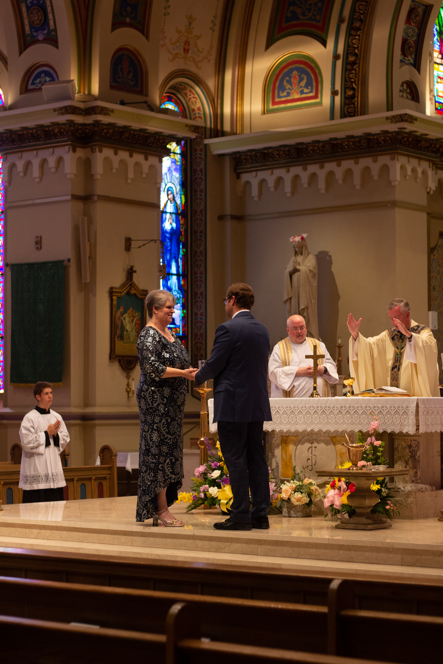 A man and woman stand at the altar of a Catholic church as priests in vestments look on during a liturgical celebration.