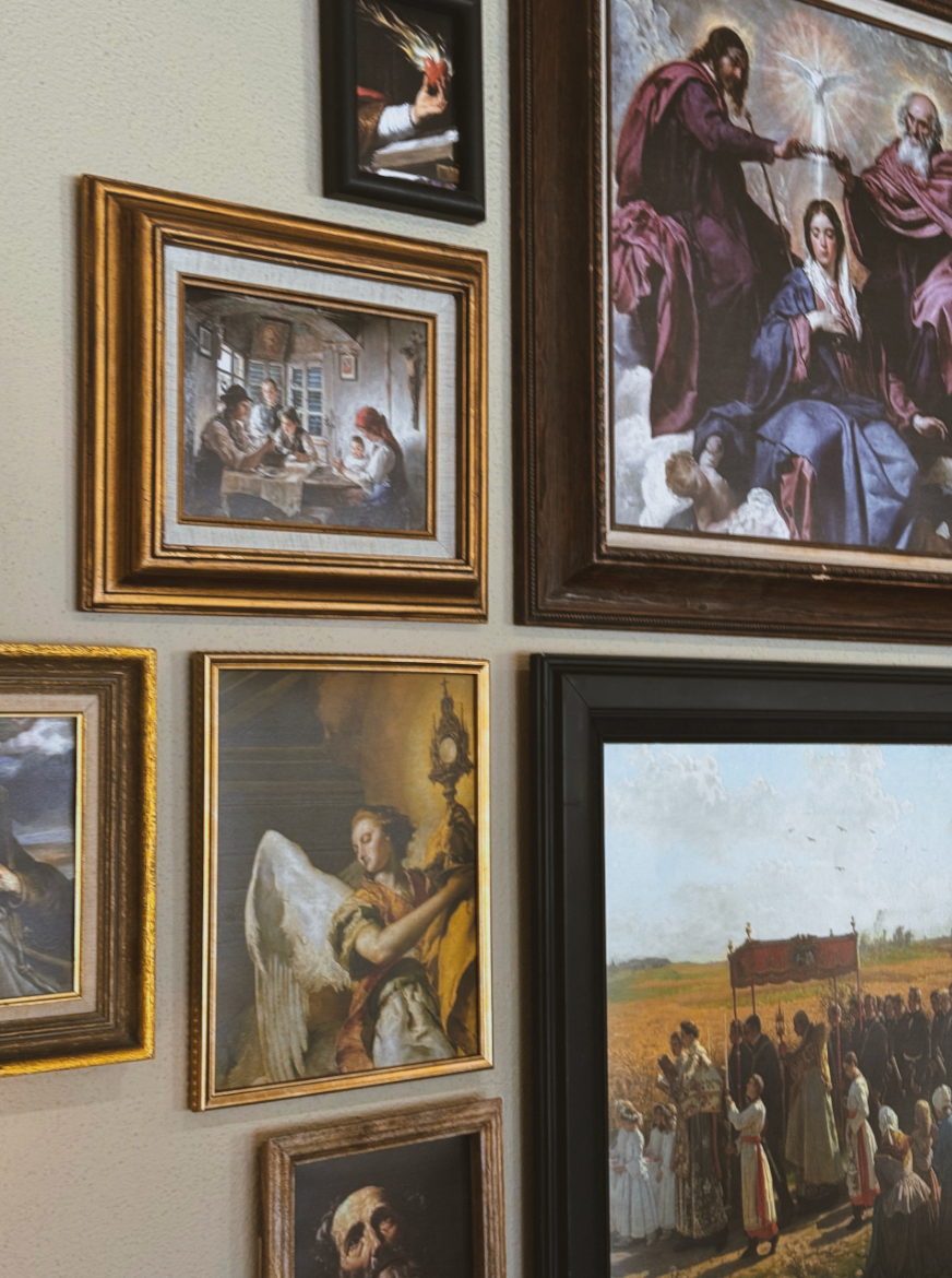 A gallery wall of framed religious oil paintings in ornate gold and dark wood frames, featuring angels, saints, and sacred scenes.