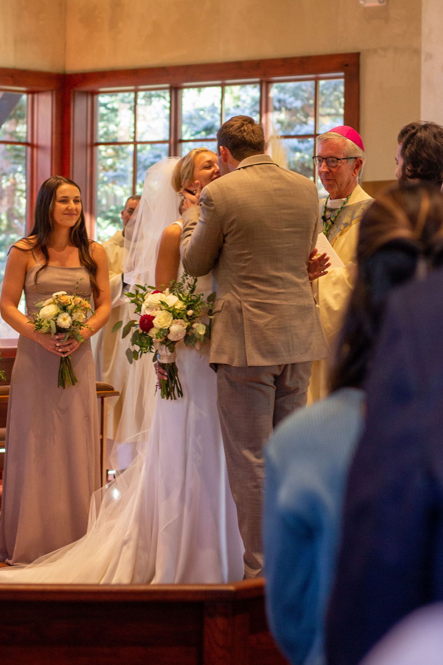 A bride and groom share an intimate moment at the altar as a bridesmaid holding a bouquet. Catholic wedding