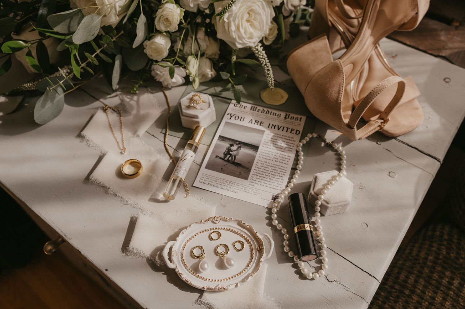 Vintage wedding details with white roses, rings, and calligraphy supplies arranged on a white tablecloth.
