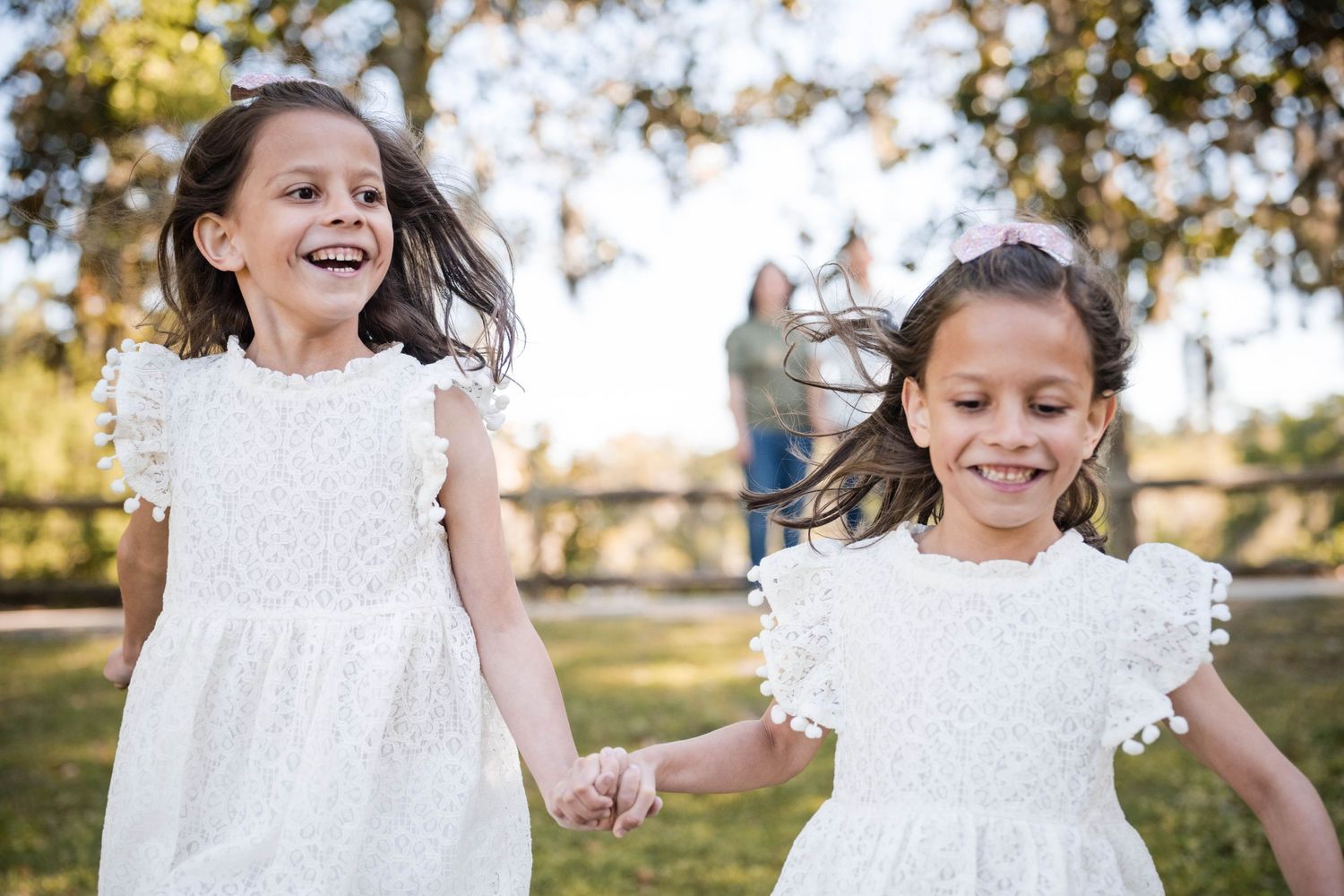 Children in white dresses playing and running together in a sunlit outdoor setting.